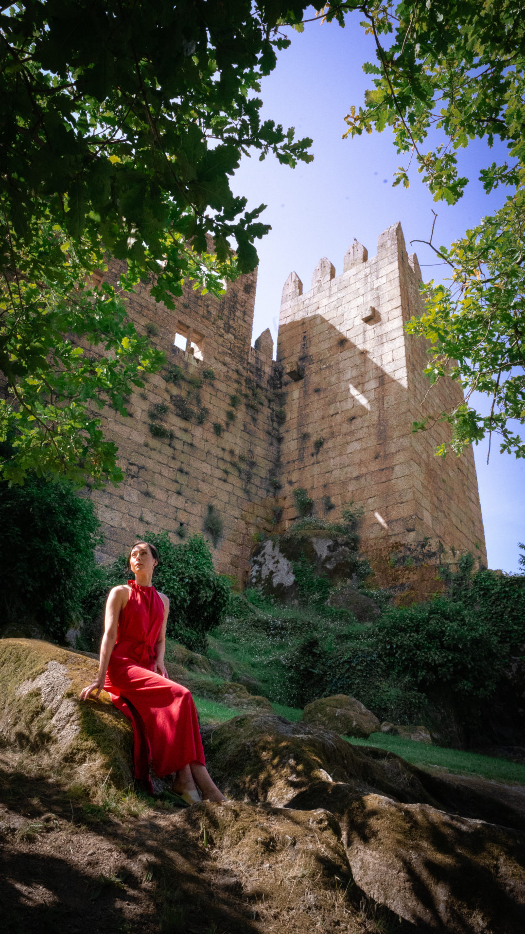 Princess Bride Travel Guide: Travel Blogger Jordan Gassner sitting on a rock in a red dress outside Guimarães Castle in Northern Portugal