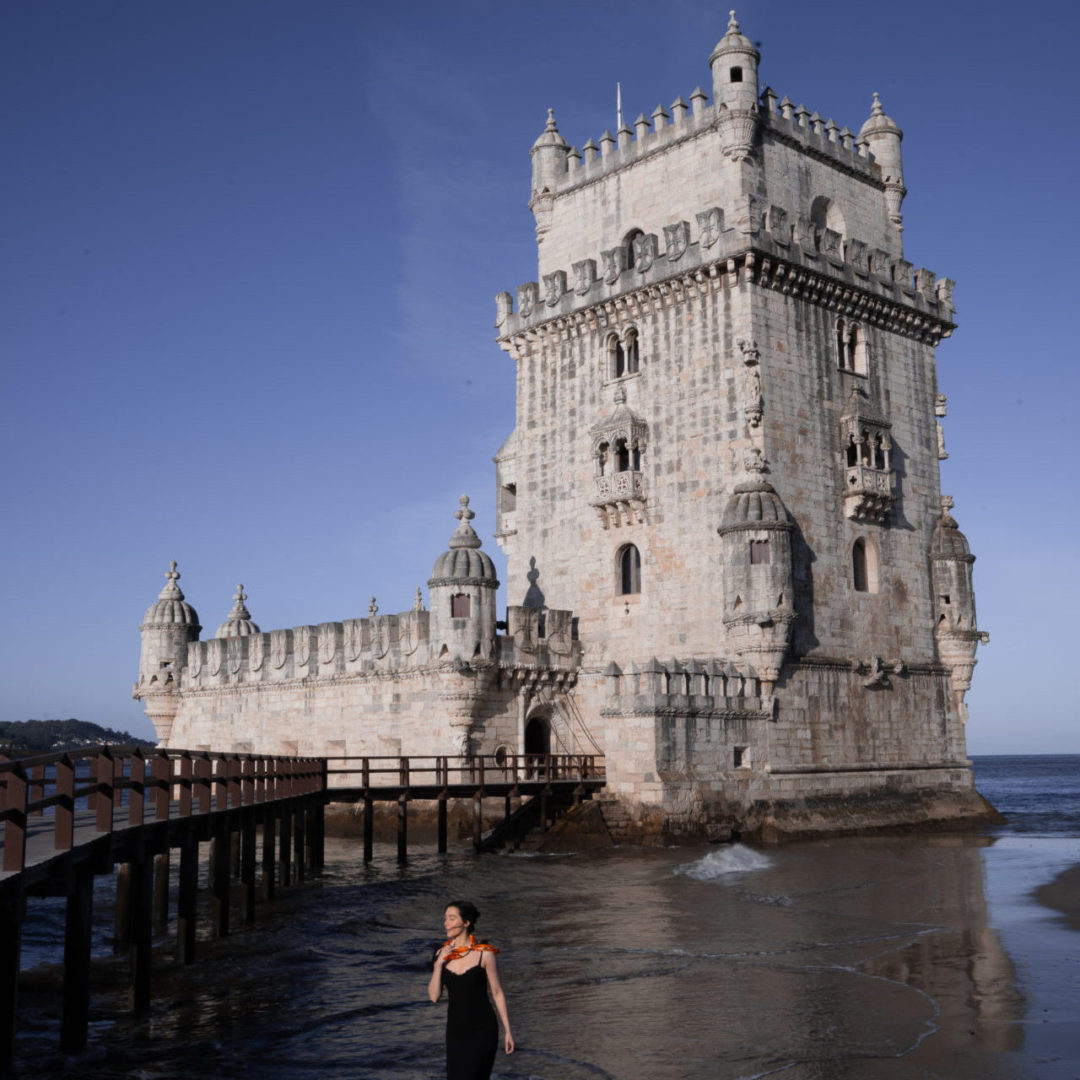 Travel Blogger Jordan Gassner walking along the beach in front of Belem Tower in Lisbon, Portugal