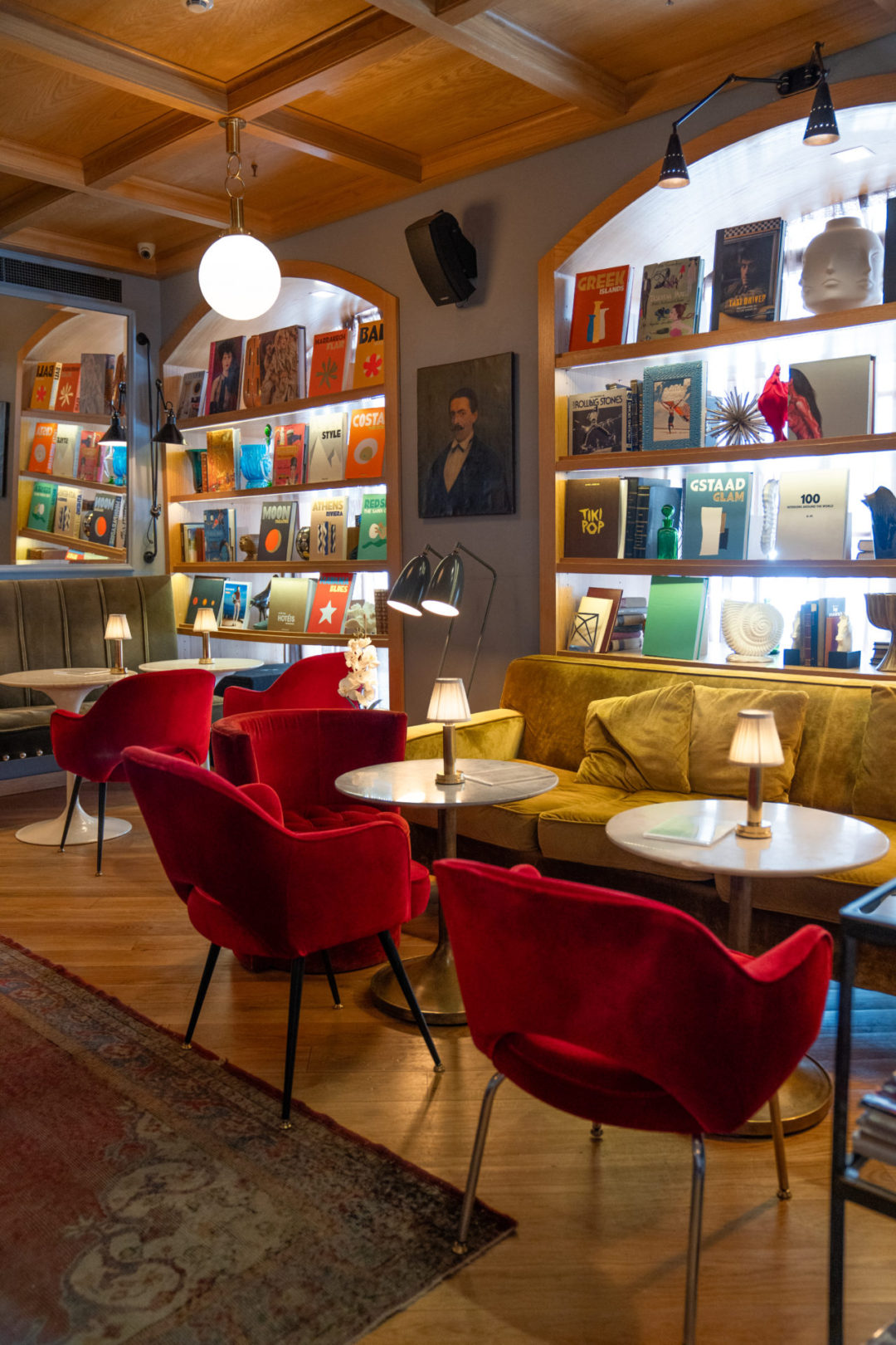 A yellow velvet sofa and set of chairs against a bookcase with full of colorful coffeetable books inside Browns Central Hotel