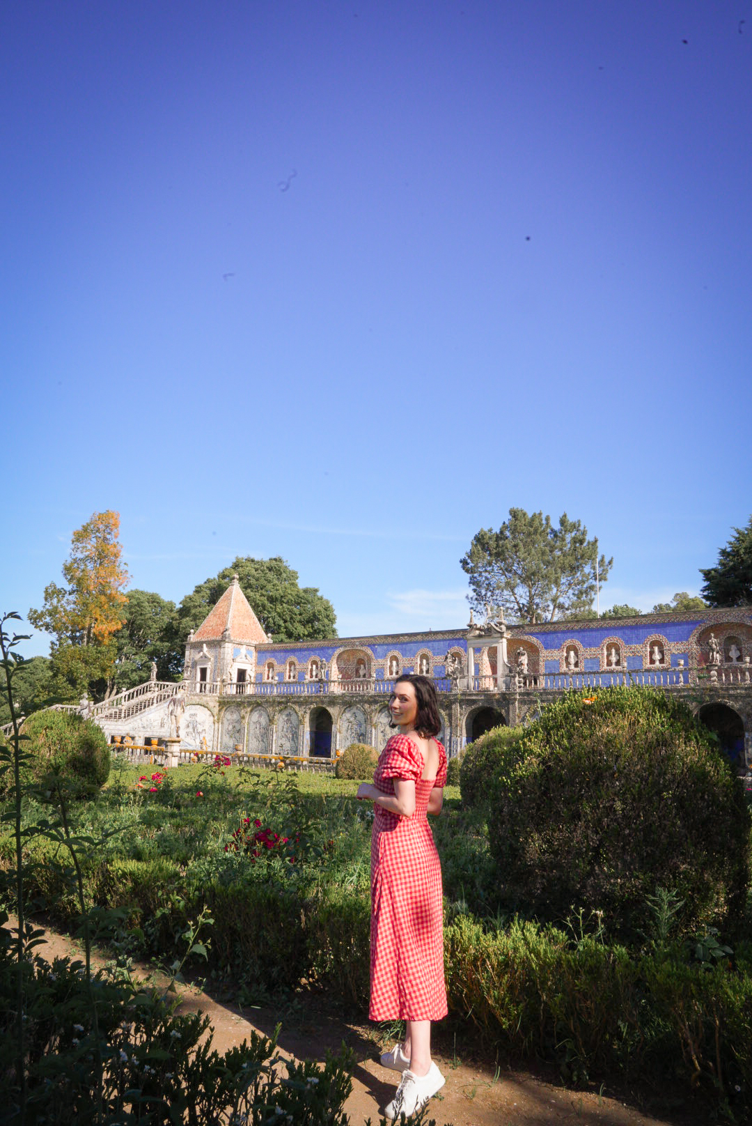 Travel Blogger Jordan Gassner looking over her shoulder and smiling along a pathway in the Palace Fronteira Gardens in Lisbon, Portugal