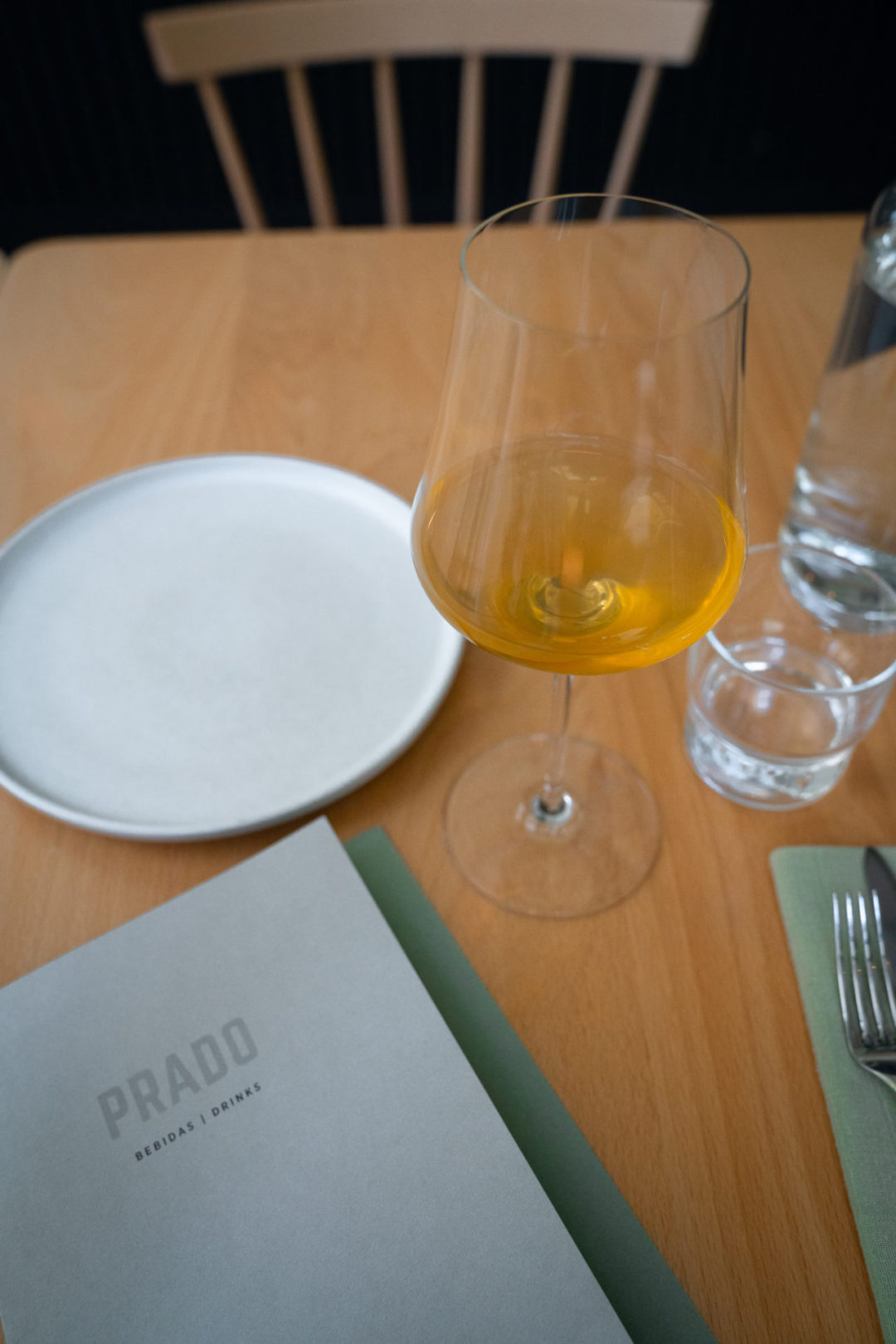 A glass of orange wine next to a green and white place setting menu at Prado Restaurant in Lisbon, Portugal