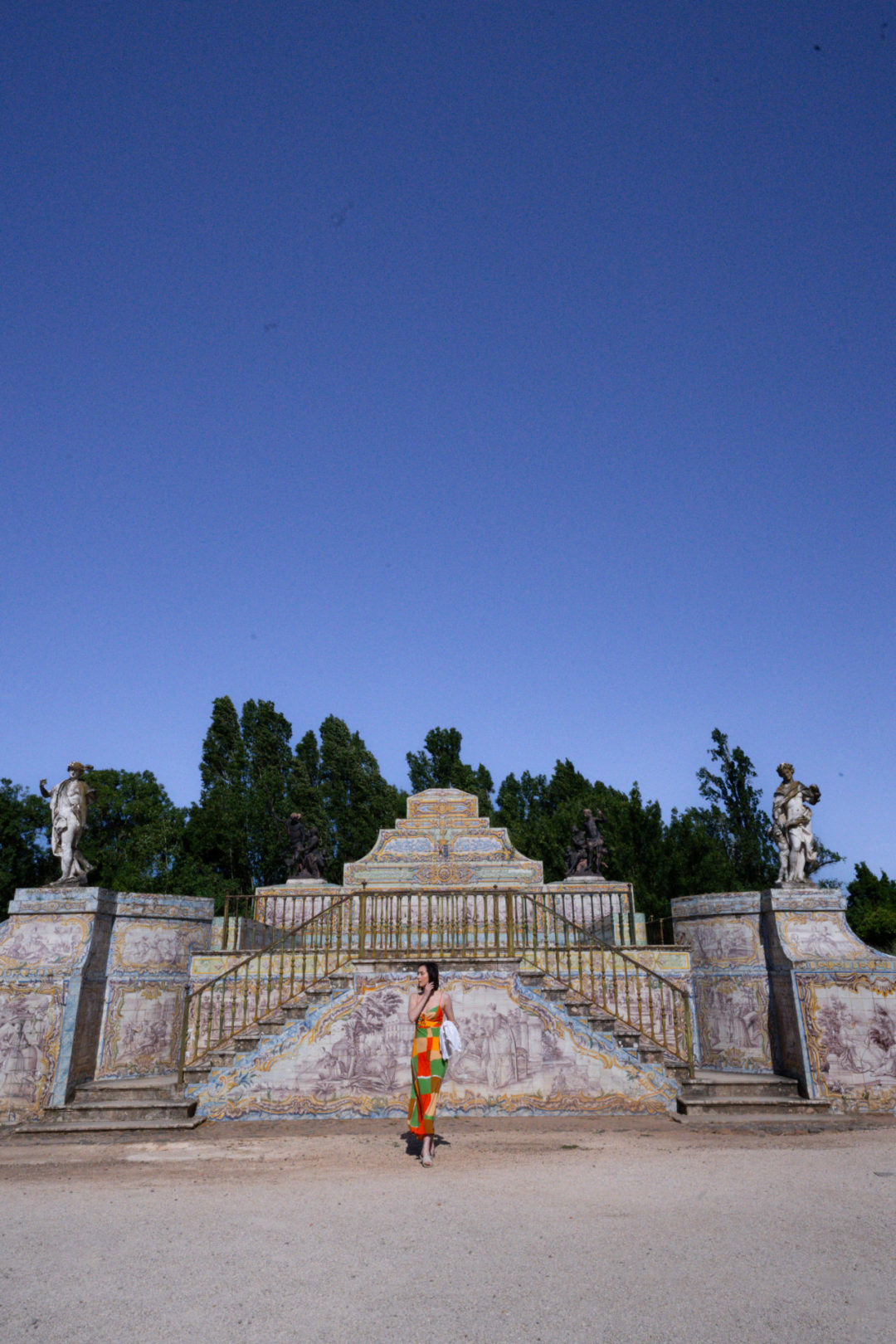 Travel Blogger Jordan Gassner looking left and over her shoulder in front of a staircase leading to a pool outside of Queluz Palace in Lisbon, Portugal