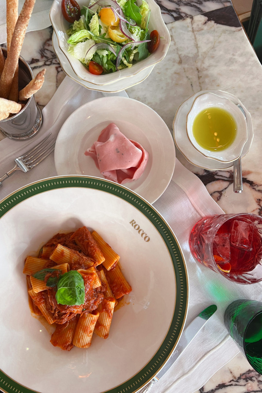 Colorful plates of pasta, cold cuts, and salad next to a Negroni from Rocco Gastrobar in Lisbon, Portugal