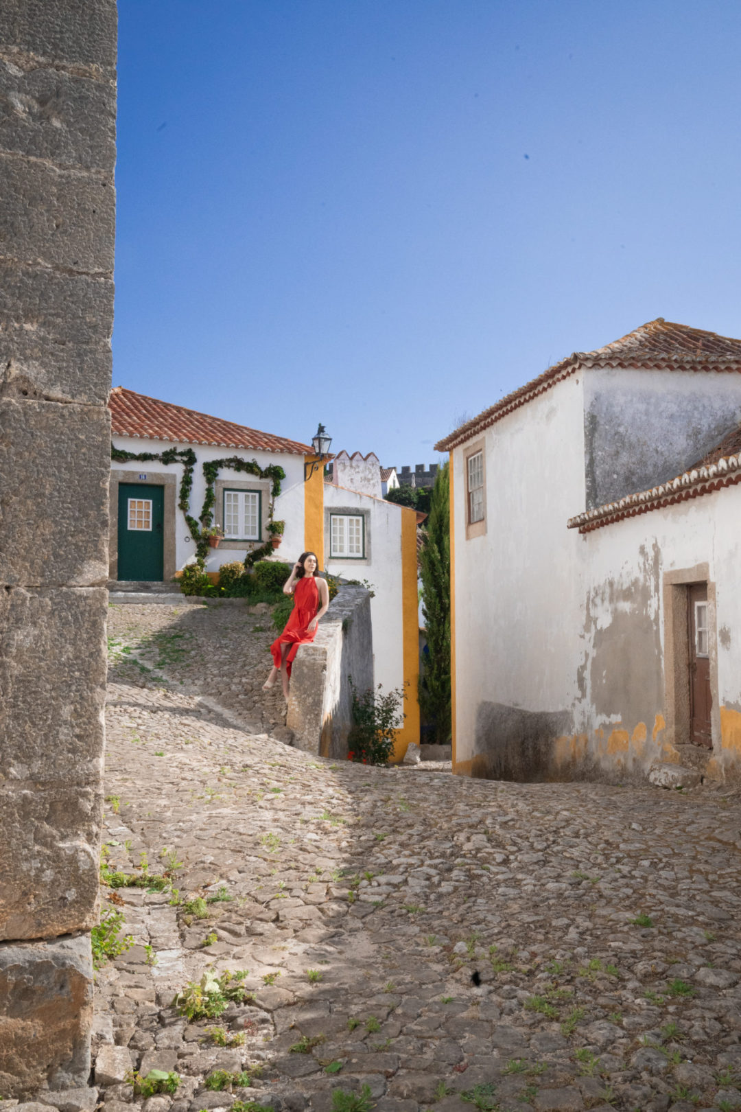 Travel Blogger Jordan Gassner sitting along a wall at a crossroads going up and down in Obidos, Portugal