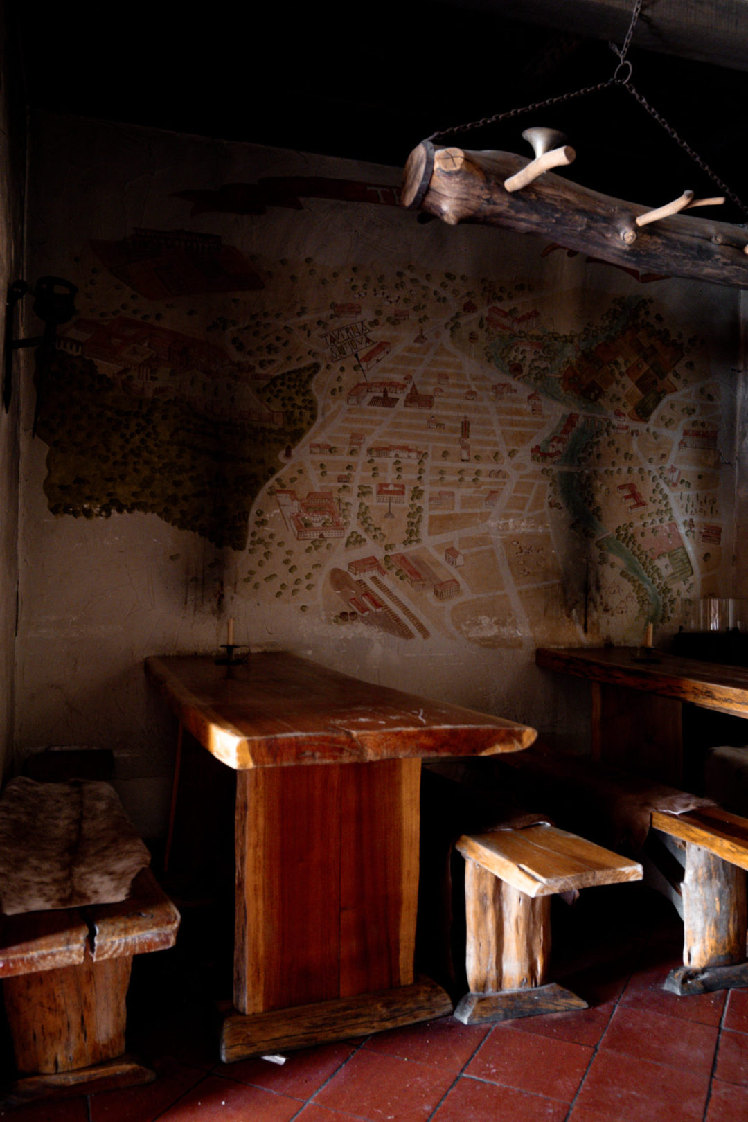A row of wooden seats and faux furs next to a wall with a medieval map inside the medieval themed tavern, Taverna Antica, in Tomar, Portugal