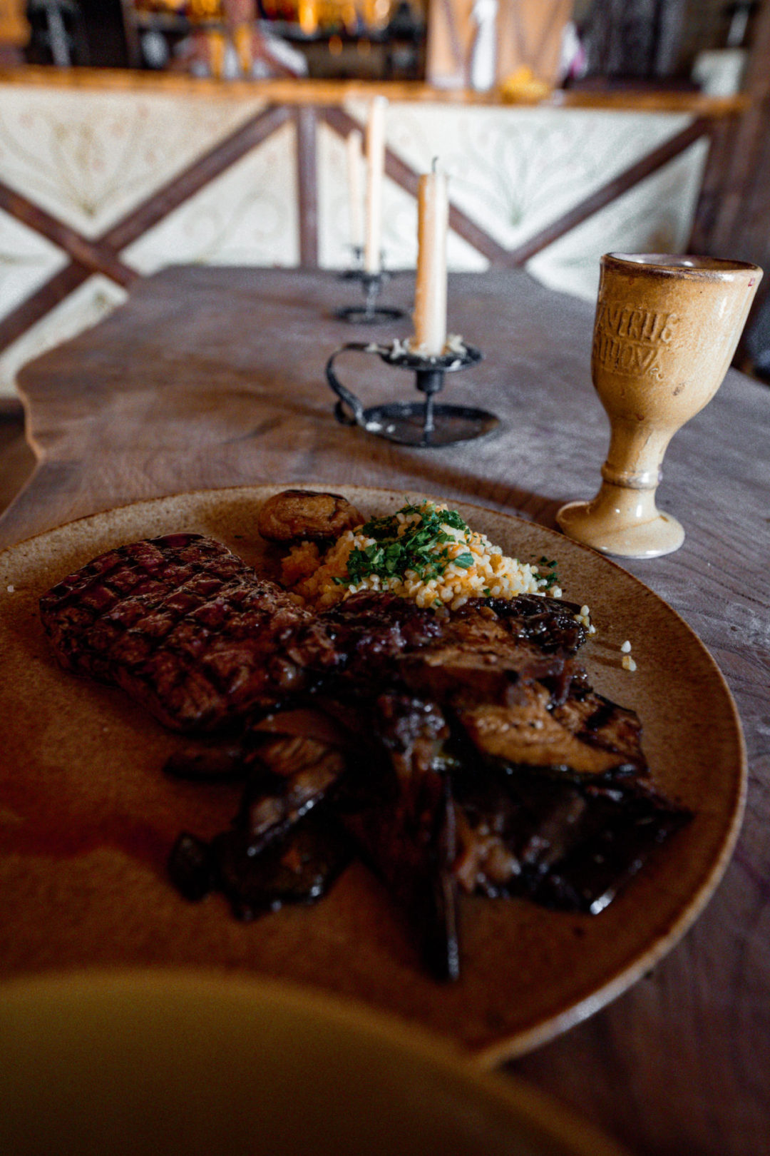 A piece of steak, root vegetables and quinoa next to a glass of wine on a table inside the medieval-themed restaurant Taverna Antiqua in Portugal