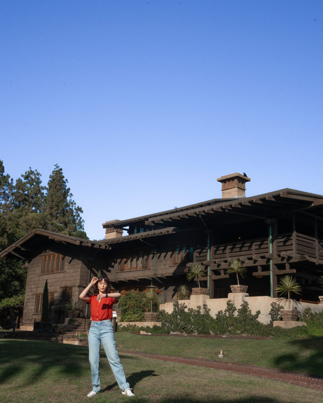 Travel Blogger Jordan Gassner pulling up her sunglasses to look at the time on her watch while dressed like Marty McFly outside the Gamble House in Pasadena