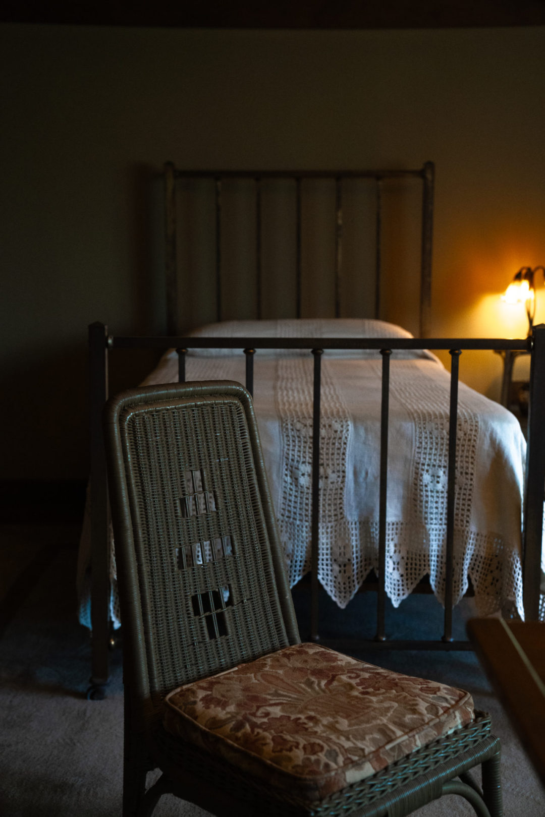 Home Tours in Los Angeles: An iron bed and patterned wicker chair inside a bedroom in Pasadena's Gamble House