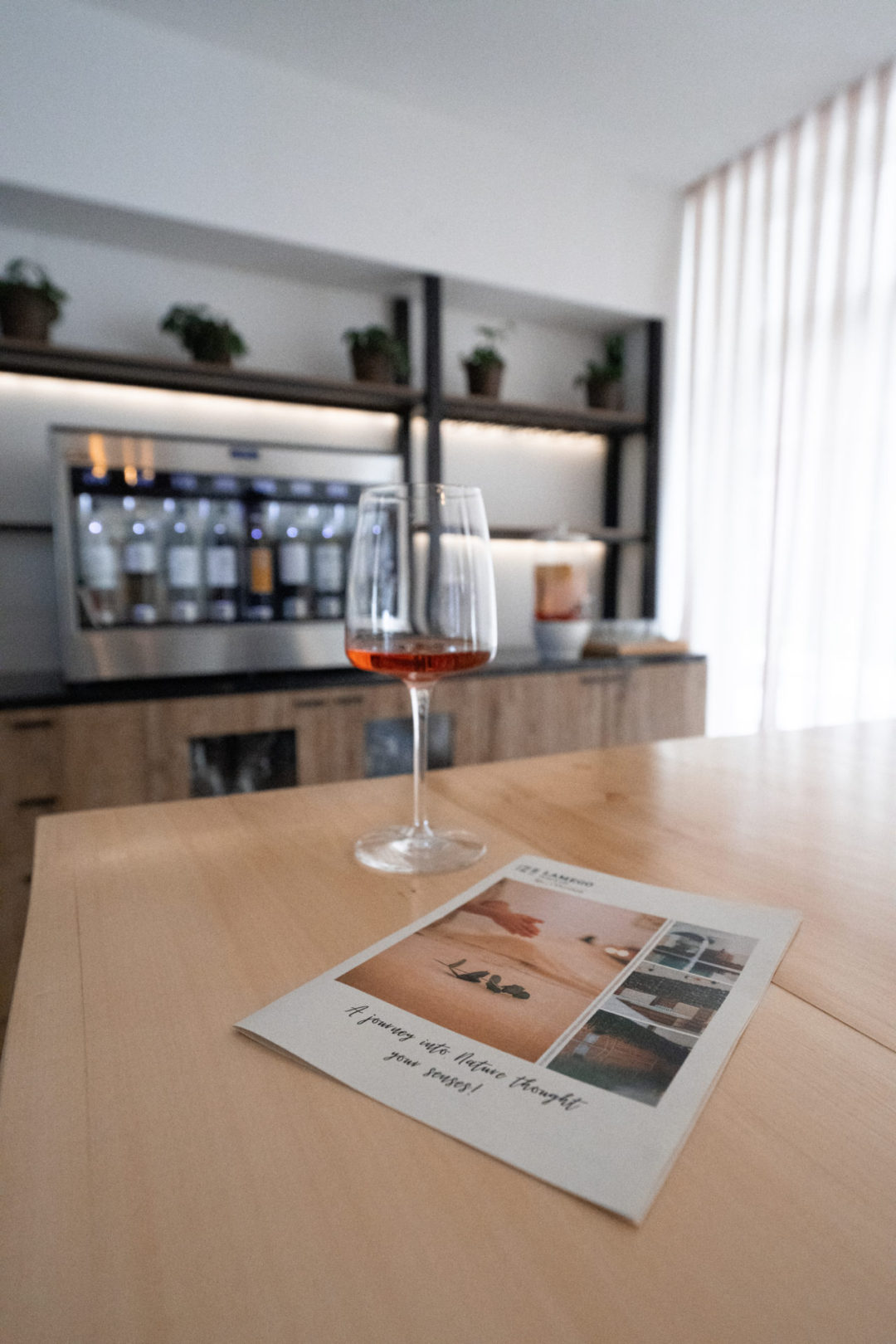 A glass of rose and welcome guide on a table in front of machine offering 8 wines on tap inside Lamego Hotel and Life in Portugal
