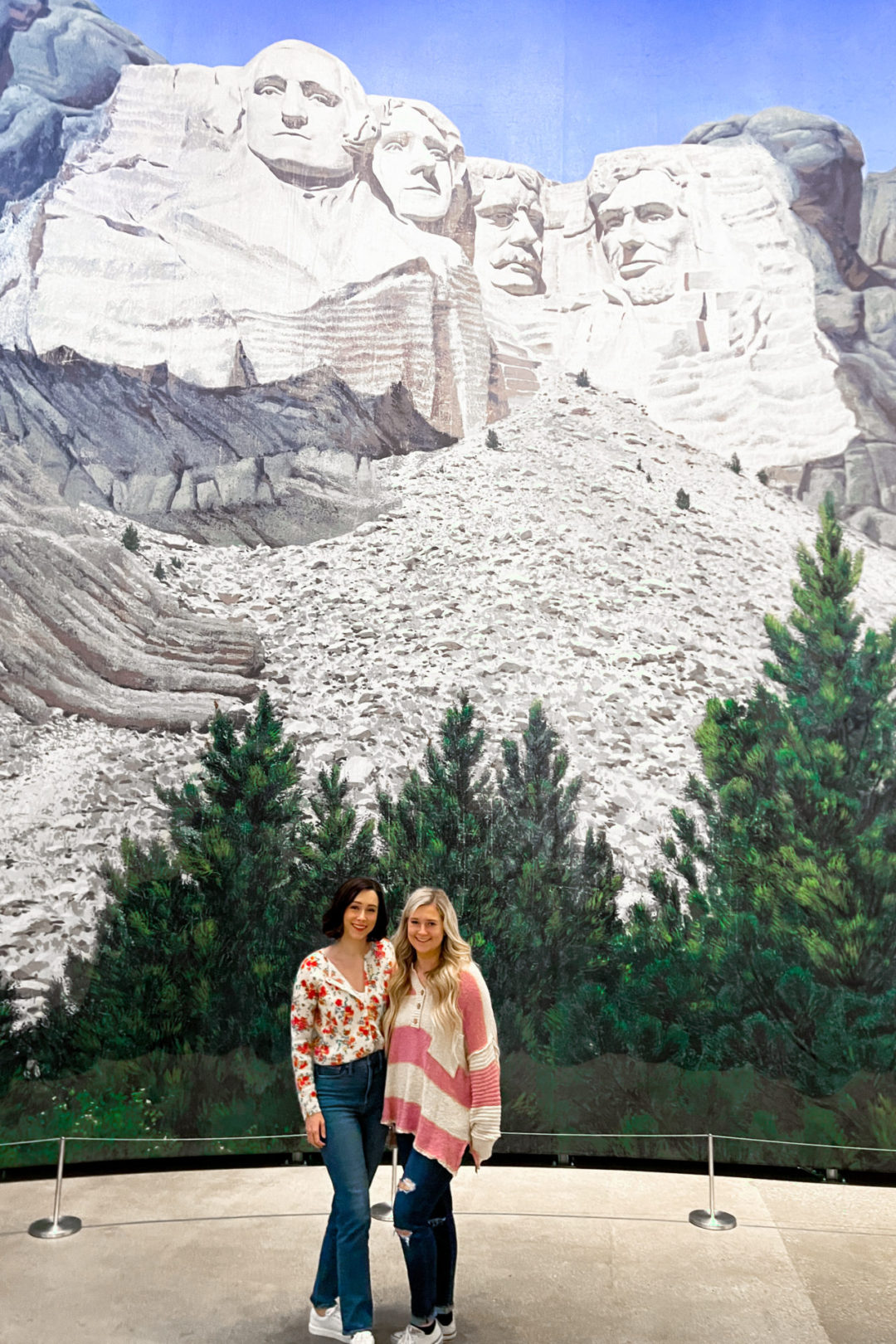 Travel Blogger Jordan Gassner and her sister standing and smiling in front of the North By Northwest Mount Rushmore backdrop at the Academy Museum in Los Angeles, California