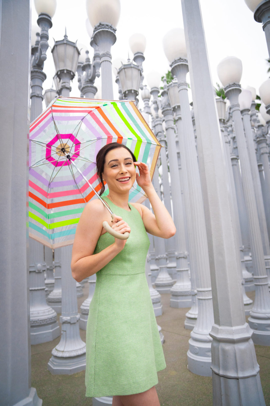 Travel Blogger Jordan Gassner smiling with umbrella under the "Urban Light" installation outside of LACMA
