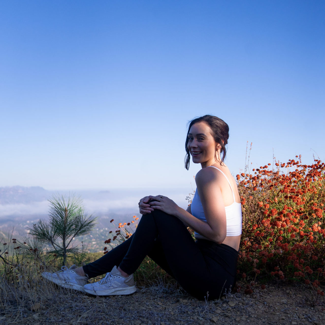 Travel Blogger Jordan Gassner smiling while sitting near a hiking viewpoint above the clouds in Topanga Canyon, California