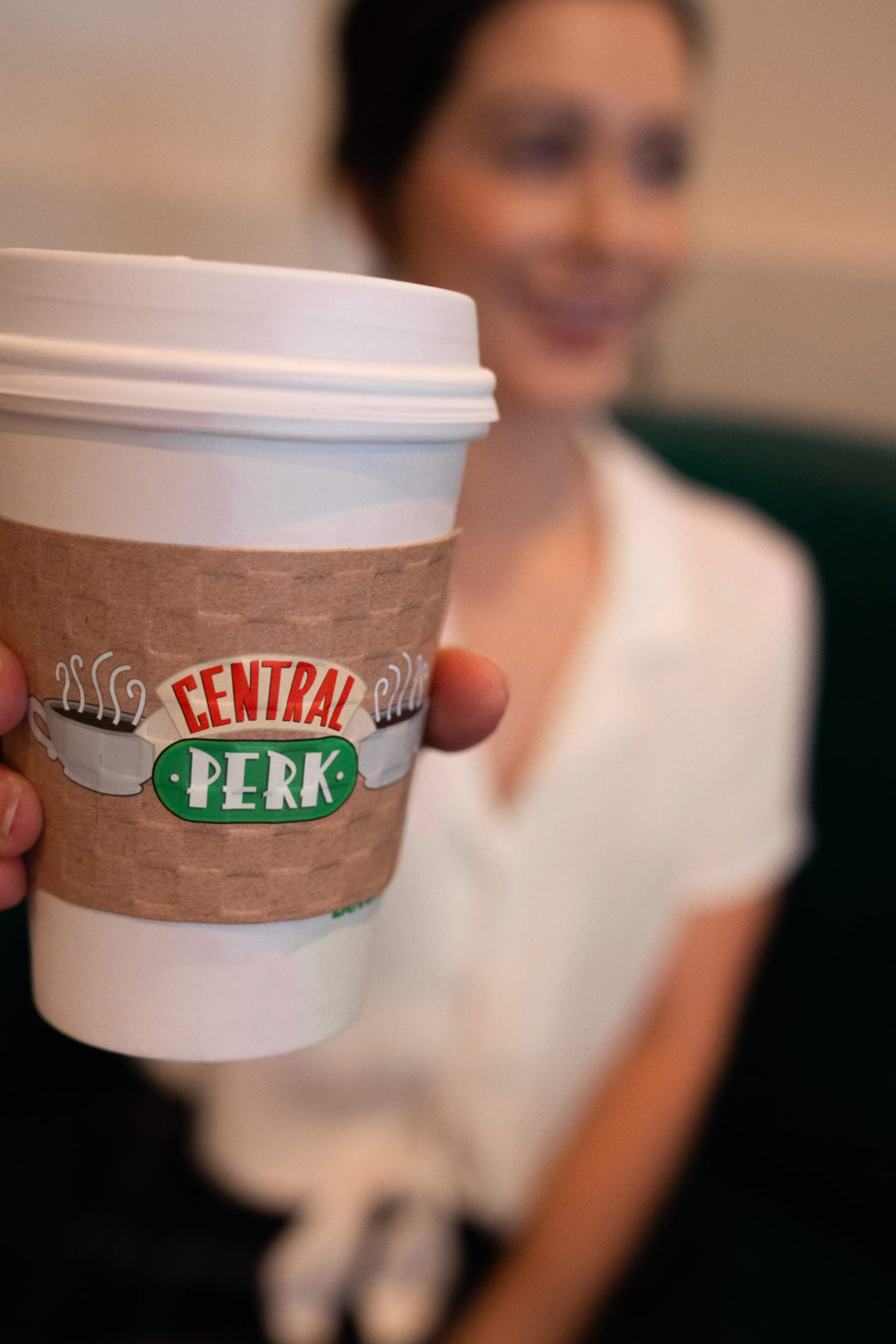 A close-up of a coffee cup with a sleeve reading "Central Perk" held by Jordan Gassner