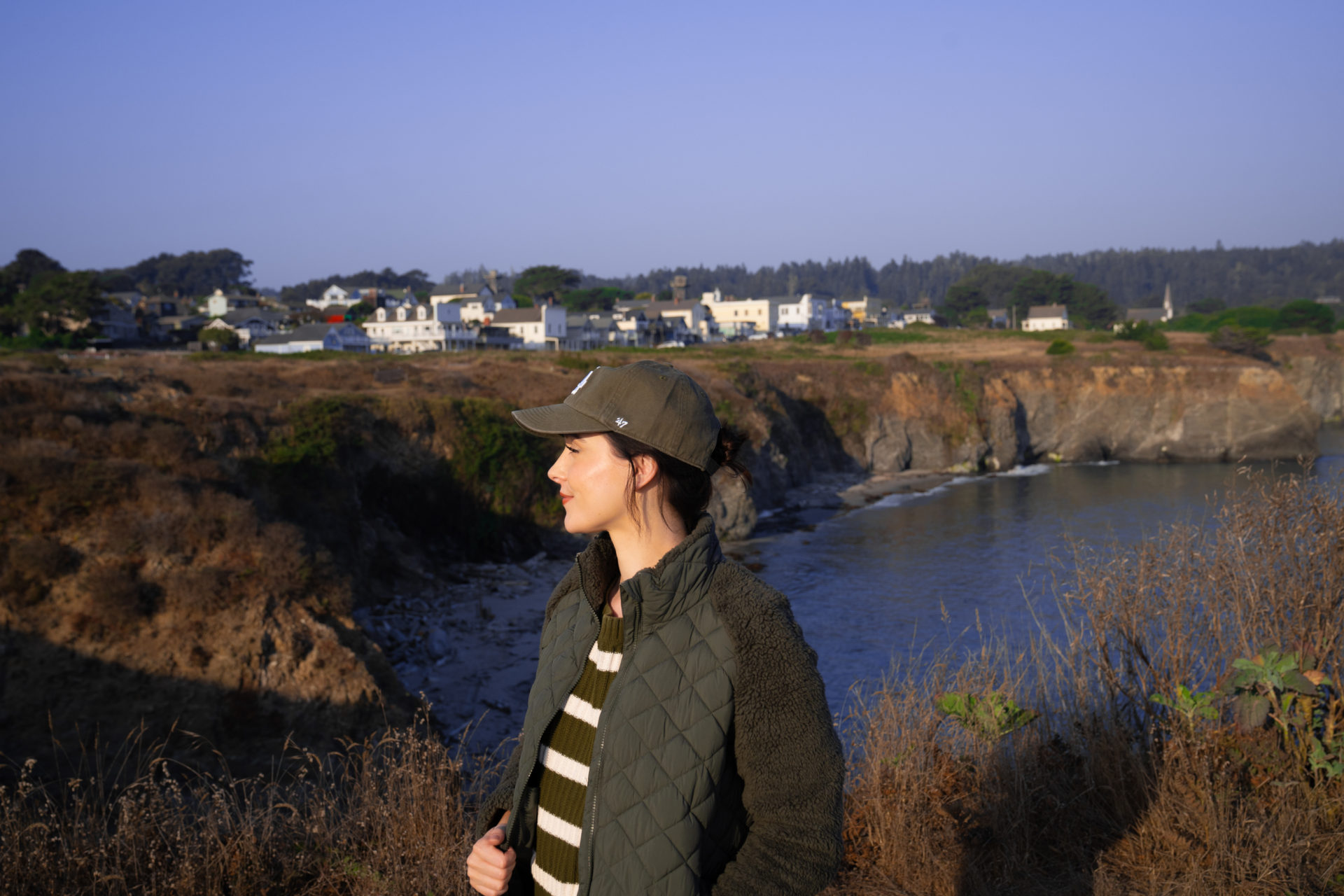 Travel Blogger Jordan Gassner looking left and smiling along the cliffside in front of the town of Mendocino, California