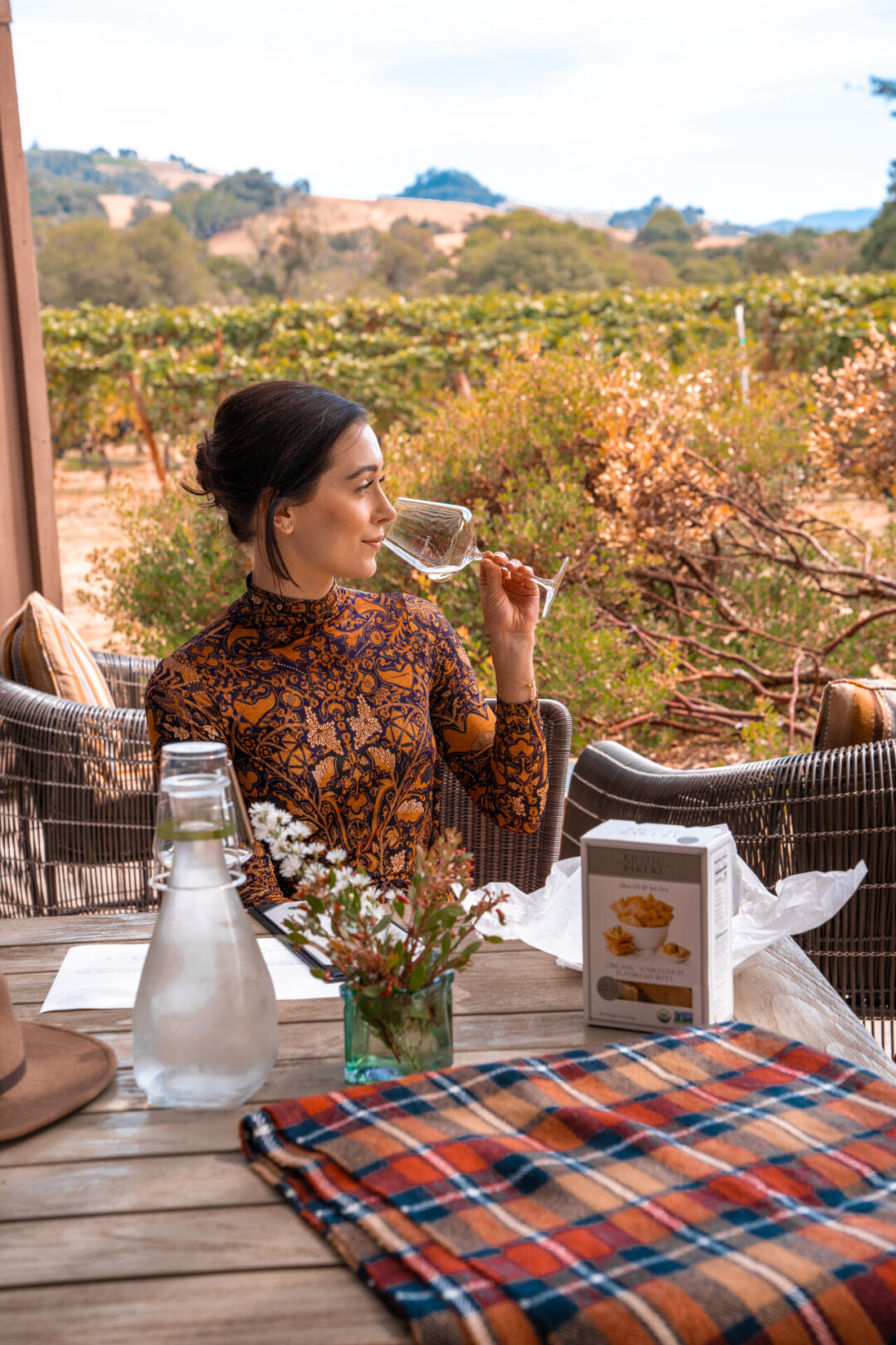 Travel Blogger Jordan Gassner drinking a glass of wine on a patio near a vineyard at Domaine Anderson Winery in Philo, California