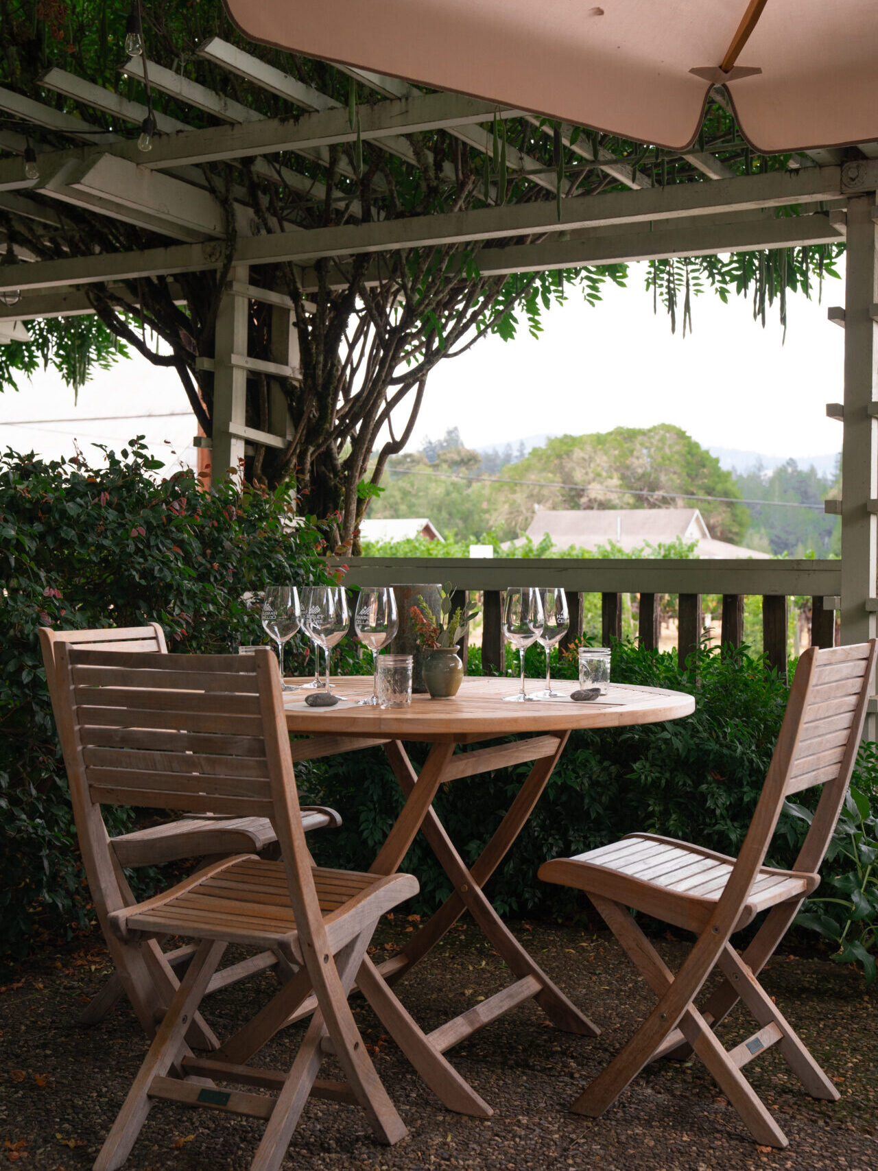 An empty table set for a wine tasting under a shaded patio overlooking a vineyard with a white barn at Handley Cellars in Northern California