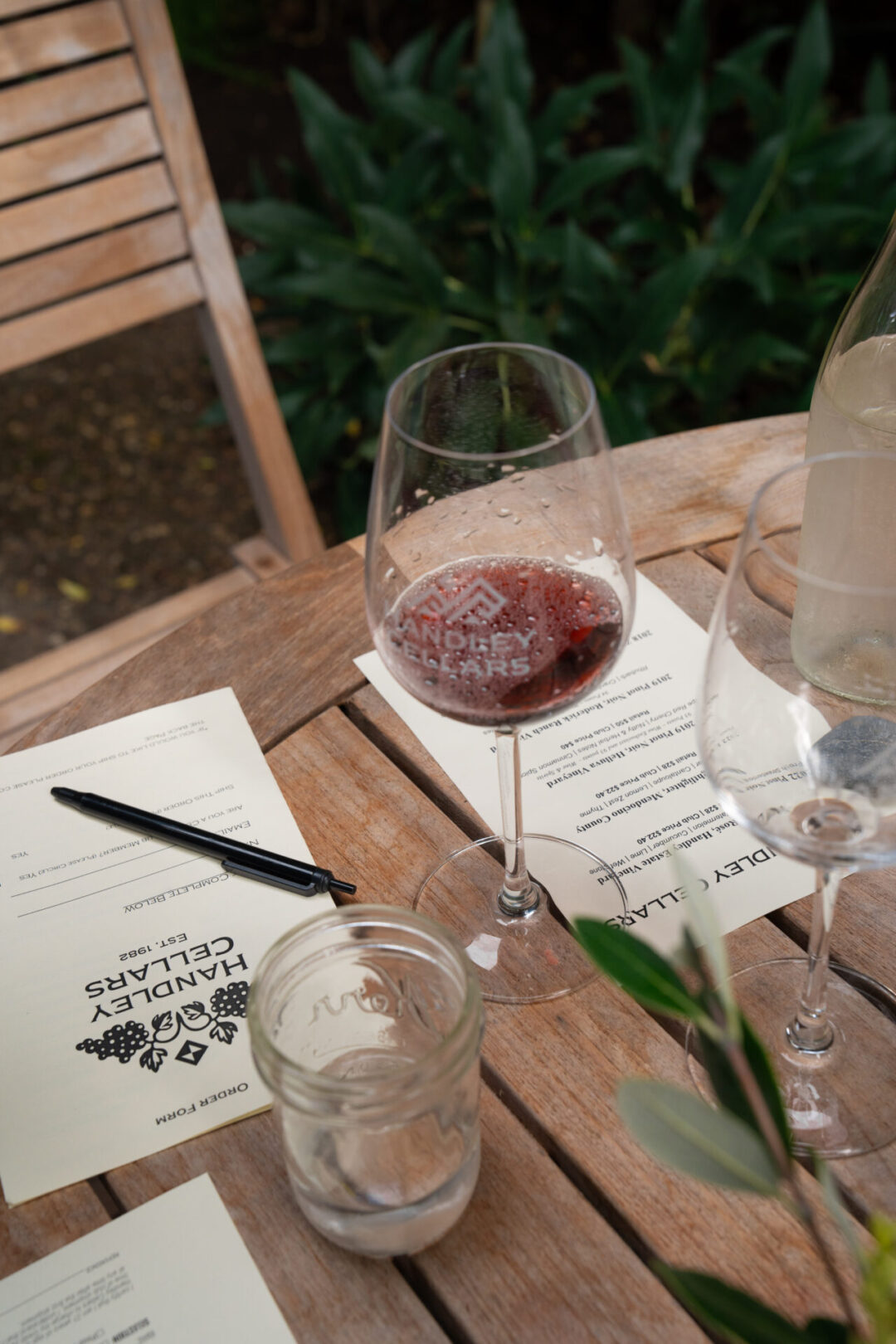 A glass of red wine in a "Handley Cellars"-labeled wine next to a tasting card and pen at a winery in California's Anderson Valley