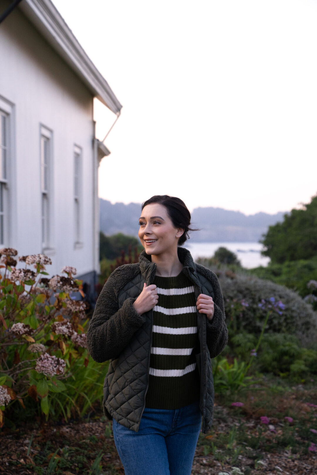 Travel Blogger Jordan Gassner smiling while bundling up in her green coat outside the historic Ford House in Mendocino, California