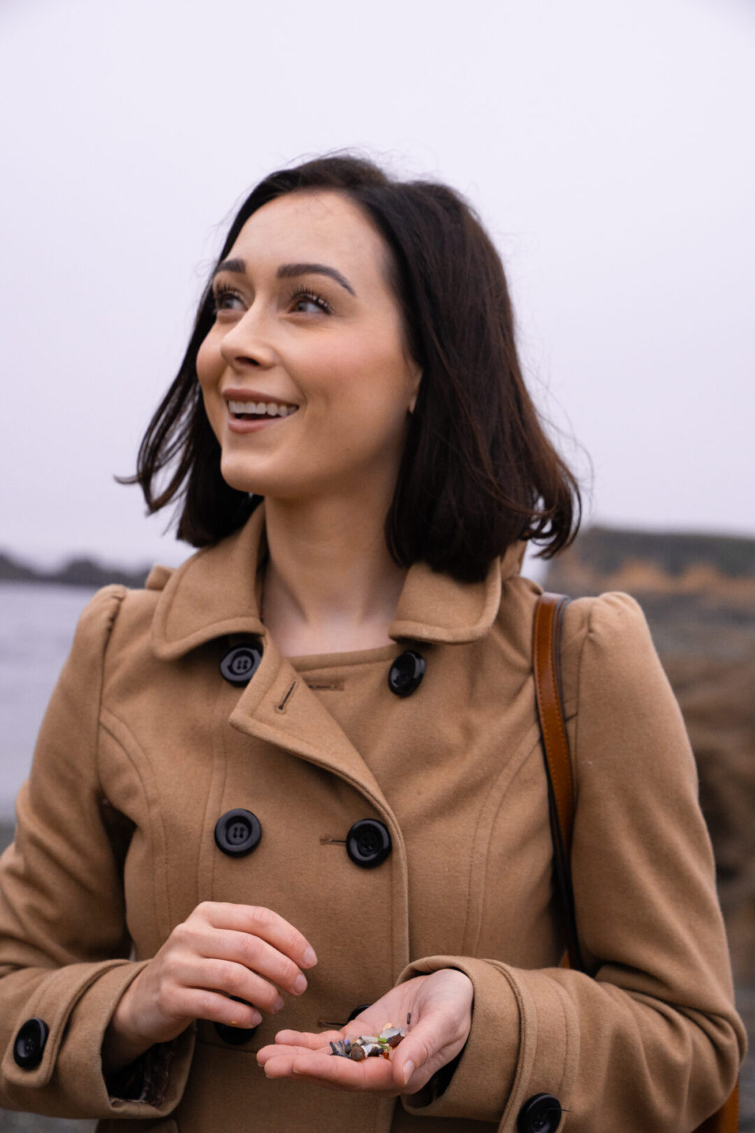 Travel Blogger Jordan Gassner smiling and looking up at the cliffs while holding some glass-sand from Glass Beach in Fort Bragg, California