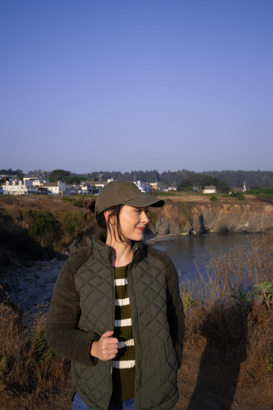 Travel Blogger Jordan Gassner looking right and smiling along the cliffside in front of the town of Mendocino, California
