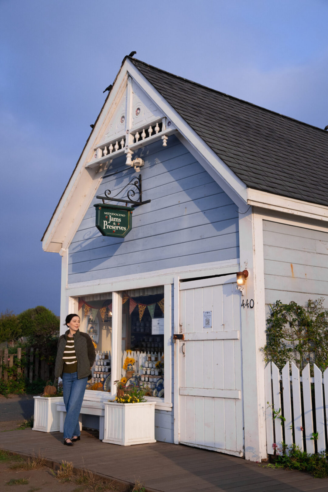 Travel Blogger Jordan Gassner standing in front of a blue Victorian building with a green "Mendocino Jams & Preserves" sign