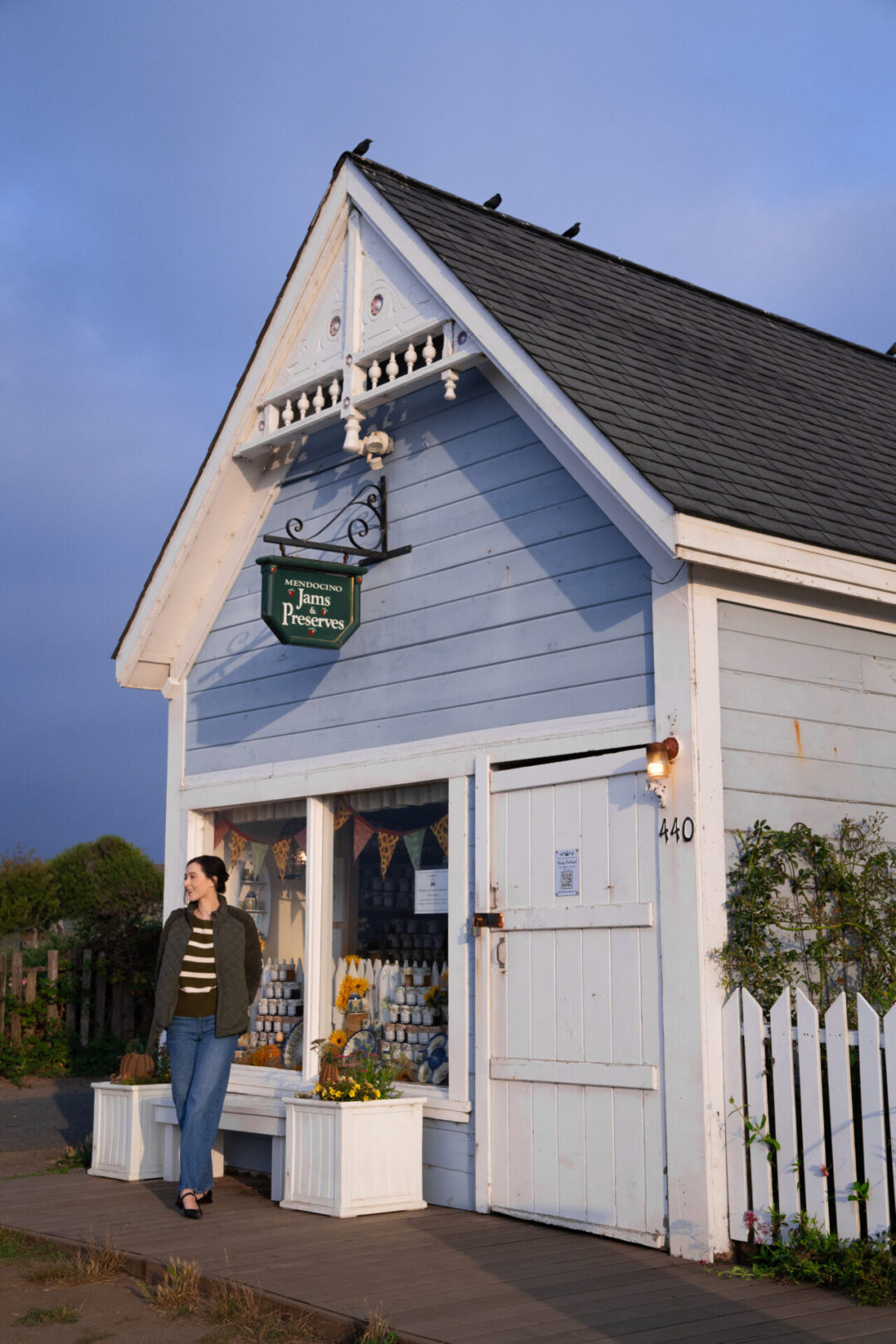 Travel Blogger Jordan Gassner walking by a blue Victorian building with a green "Mendocino Jams & Preserves" sign