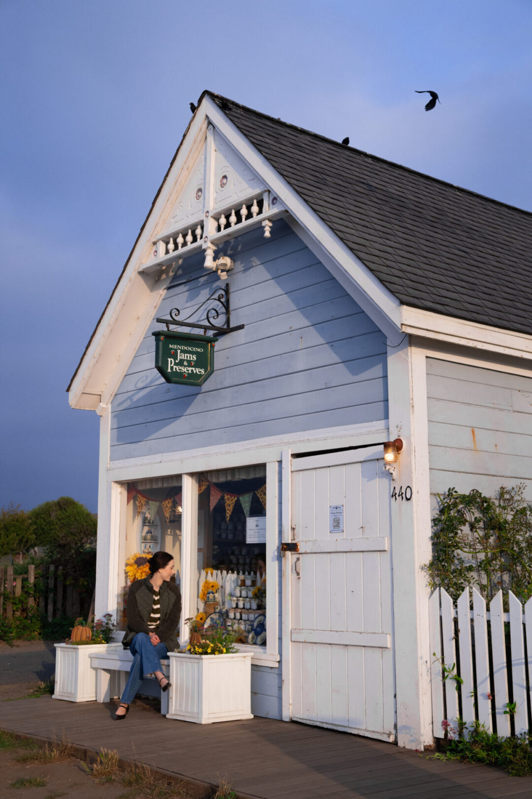 Travel Blogger Jordan Gassner looking into the window of a blue Victorian building with a green "Mendocino Jams & Preserves" sign