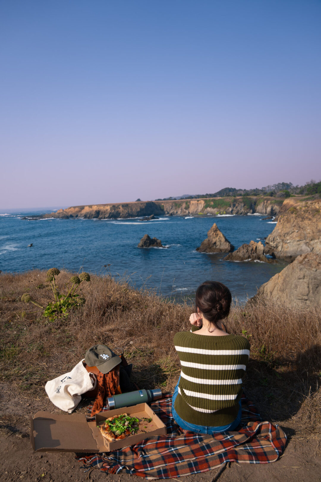 Travel Blogger Jordan Gassner sitting on a plaid blanket enjoying a picnic along the coast in Jug Handle State Natural Reserve near Mendocino, California