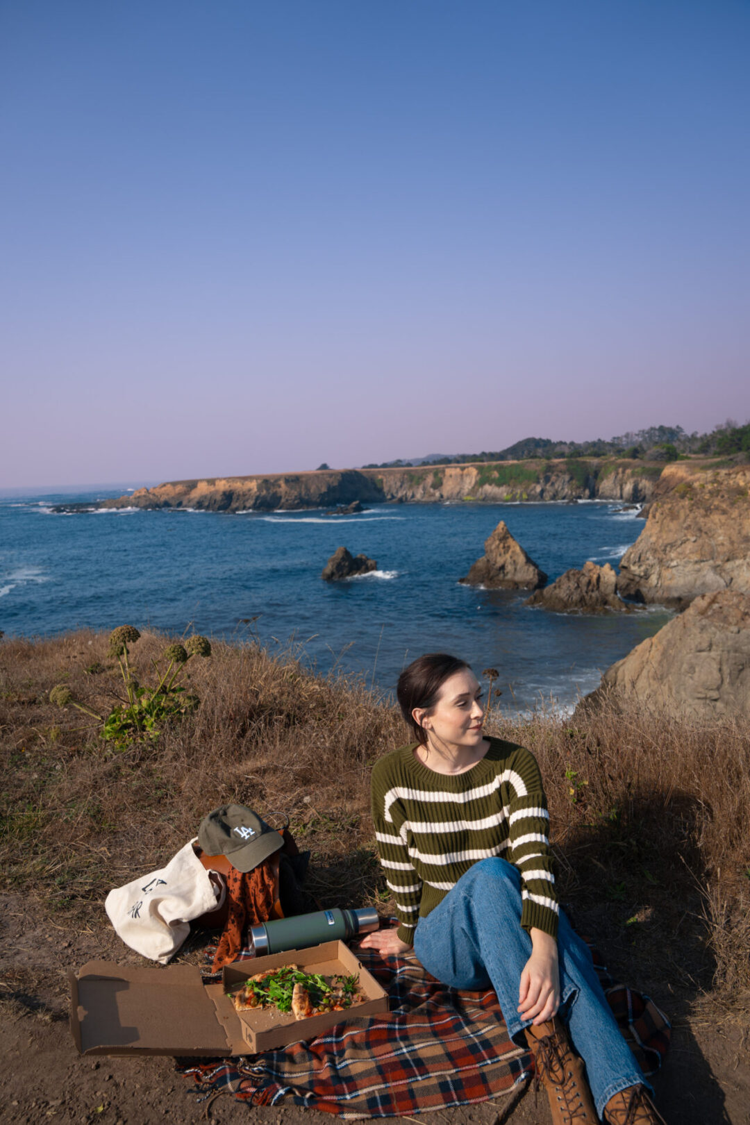 Travel Blogger Jordan Gassner sitting on a plaid blanket enjoying a picnic along the coast in Jug Handle State Natural Reserve near Mendocino, California