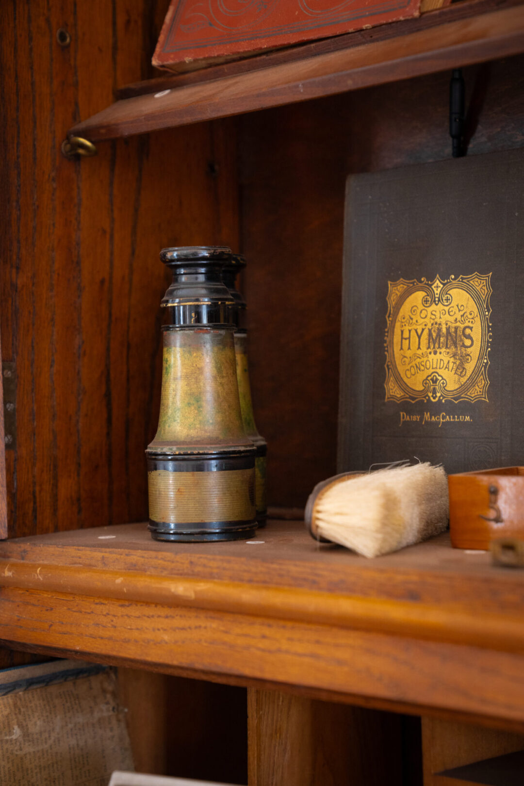 A gold and black pair of binoculars, book of Hymns and vintage brush on a shelf inside Mendocino's Kelley House Museum