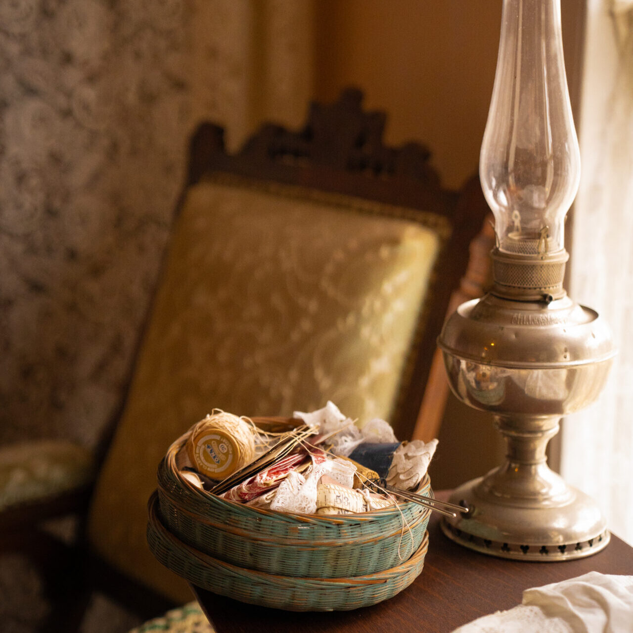 An oil lamp and a woven tray of sewing materials sitting on a side table next to a Victorian era chair inside Mendocino's Kelley House