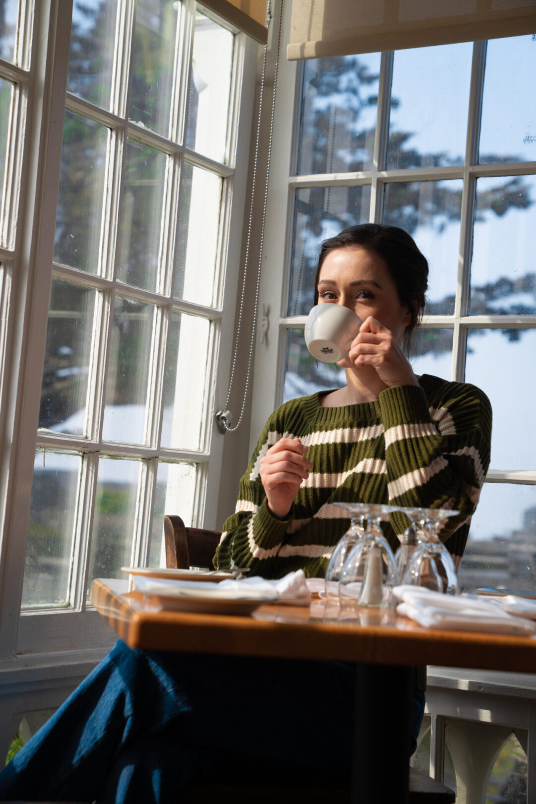 Travel Blogger Jordan Gassner drinking a cup of tea in front of a Victorian era window inside Mendocino's MacCallum House