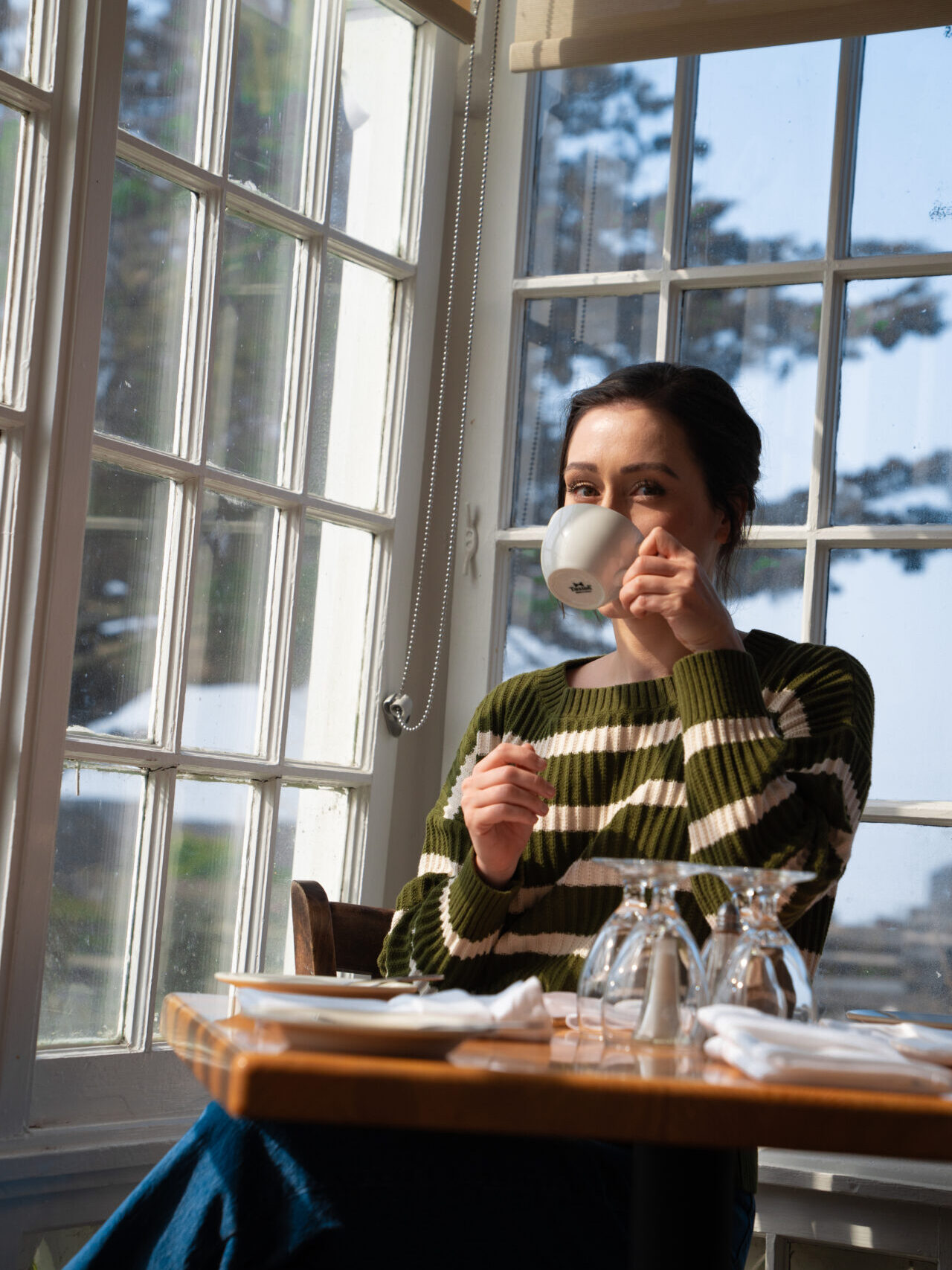 Travel Blogger Jordan Gassner drinking a cup of tea in front of a Victorian era window inside Mendocino's MacCallum House