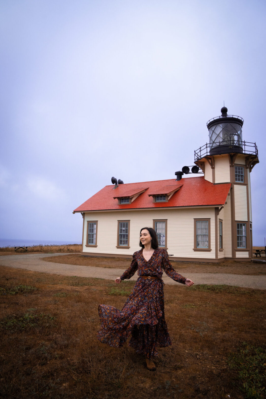 Travel Blogger Jordan Gassner smiling and twirling in front of the Point Cabrillo Light Station along the Northern California coast