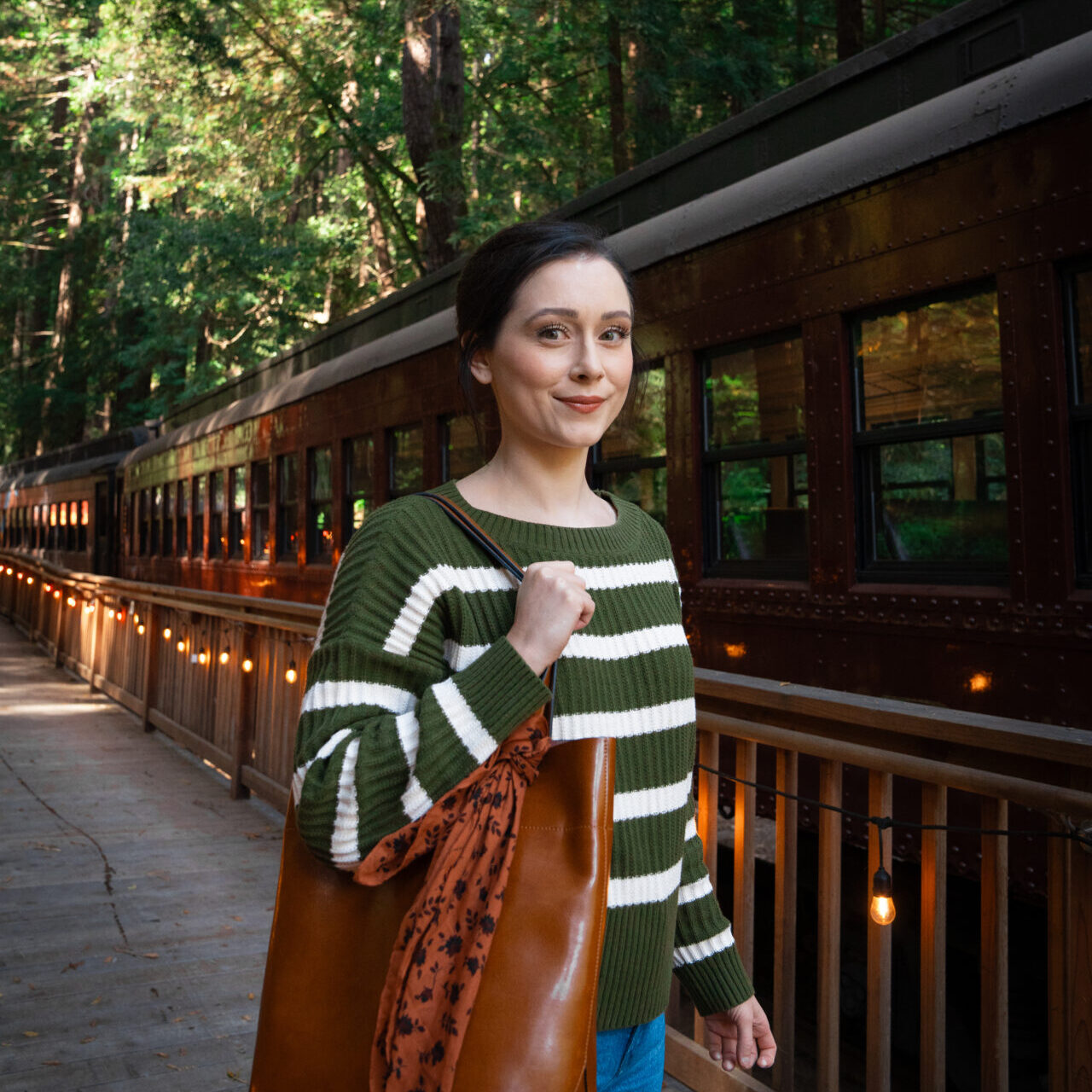 Travel Blogger Jordan Gassner holding a large brown purse on the train platform at Glen Blair Bar in Fort Bragg, California