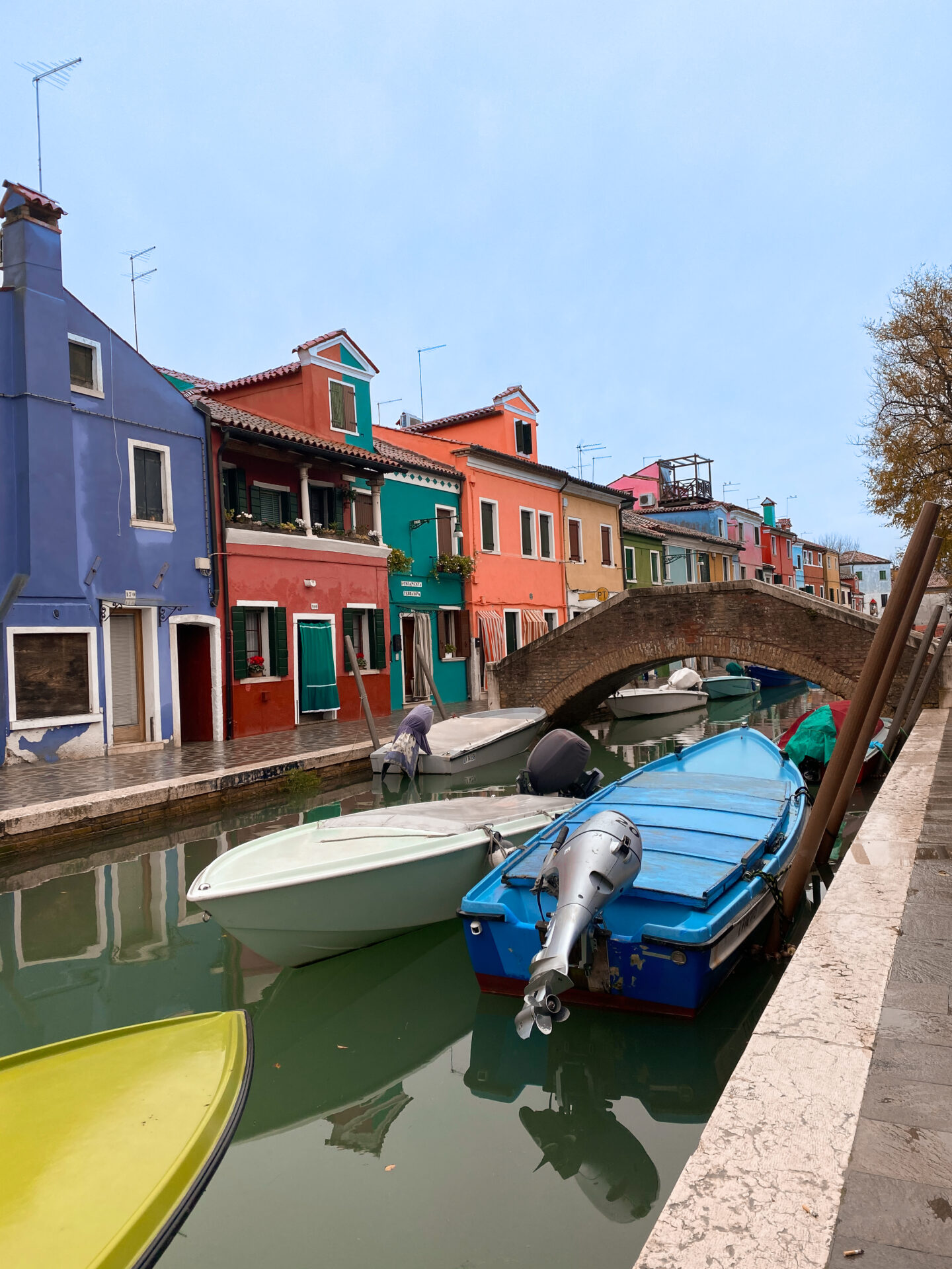 A few colorful boats in a canal with a vibrant row of houses in the background on the island of Burano near Venice, Italy