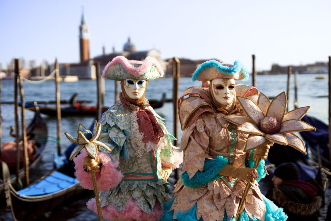 A couple standing in front of a canal in enchanting and intricately crafted costumes at Piazza San Marco during the winter Venice Carnival