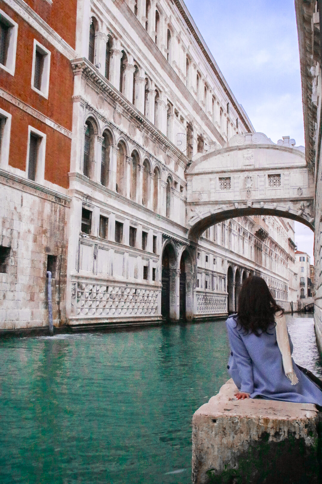 Travel Blogger Jordan Gassner sitting near a canal in Venice and looking up at The Bridge of Sighs outside of Doge's Palace
