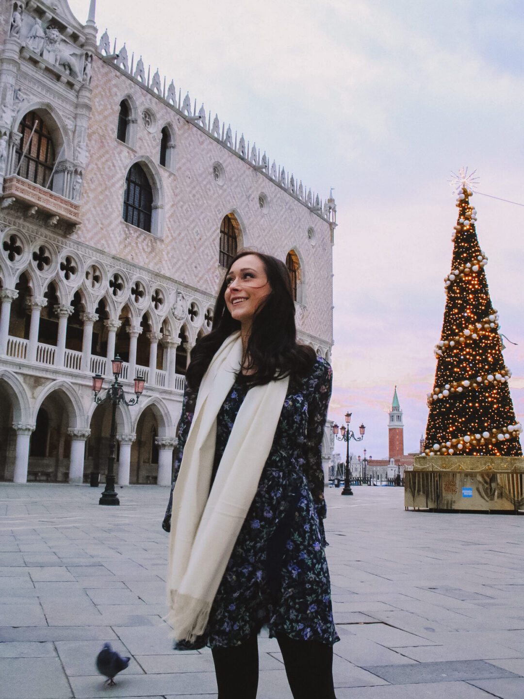 Travel Blogger Jordan Gassner smiling in front of Piazza San Marco at pink sunrise, empty save for a lit up Christmas tree