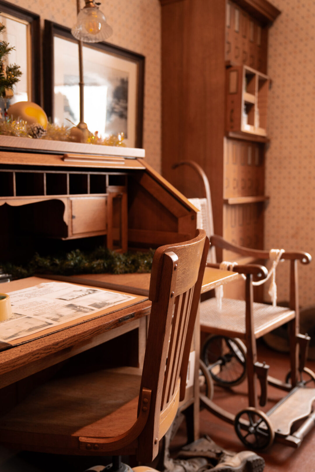 A vintage wheelchair next to a wooden chair and a desk inside the Victorian era Guest House Museum in Fort Bragg, California