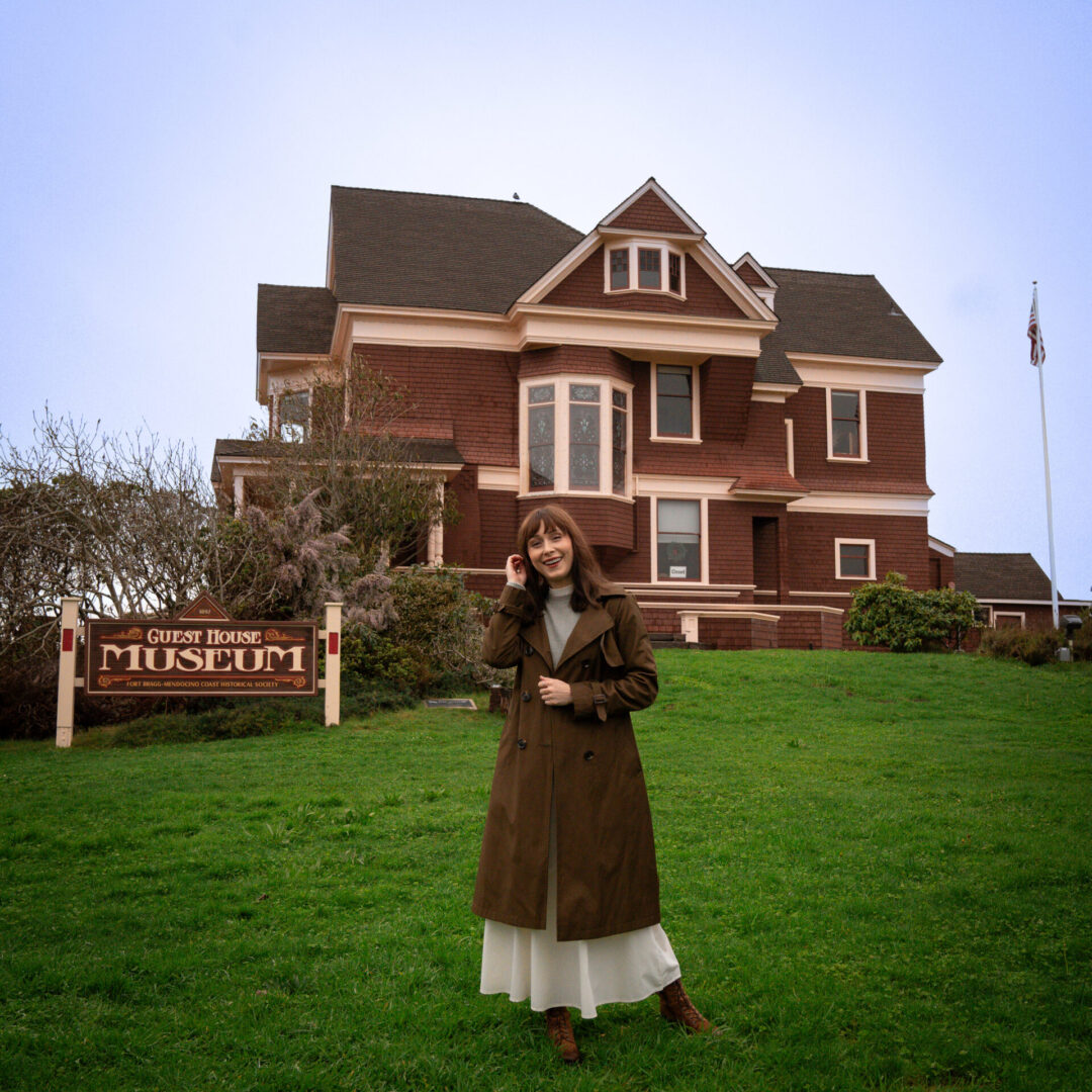 Travel Blogger Jordan Gassner smiling on the grassy hill in front of the Guest House Museum in Fort Bragg, California