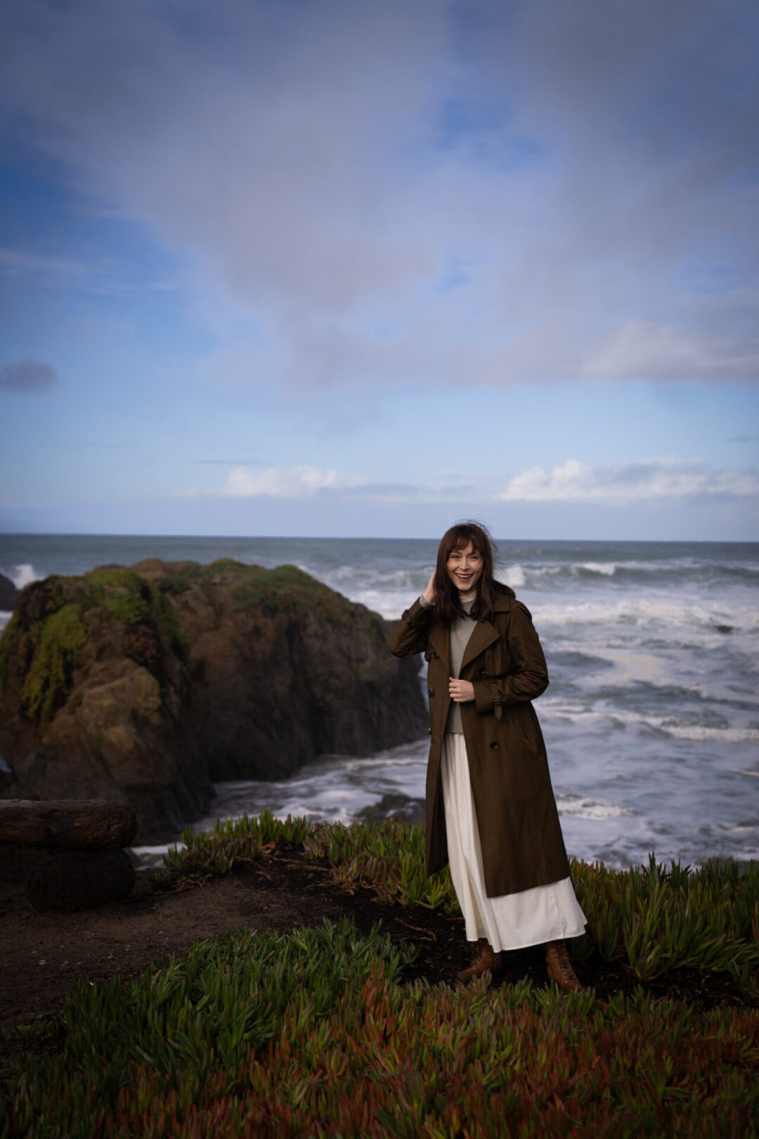 Travel Blogger Jordan Gassner smiling while bundling up in her rain jacket along Glass Beach near Mendocino, California