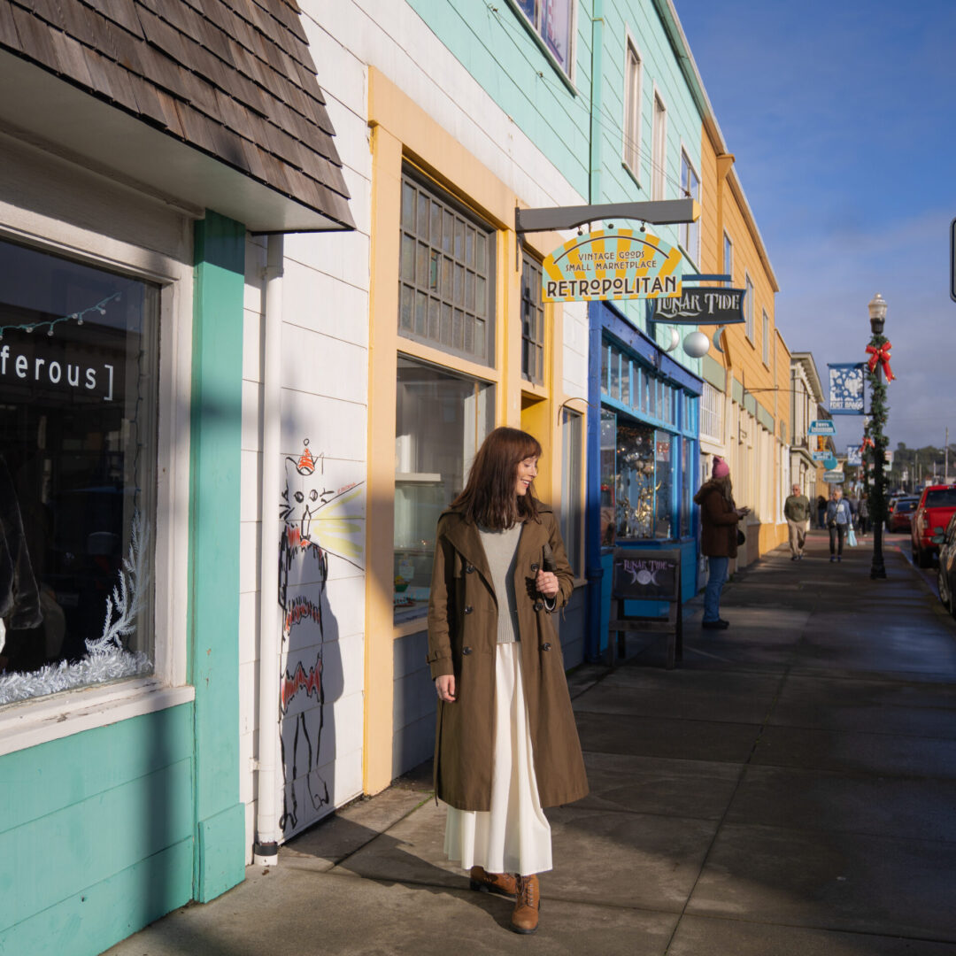 Travel Blogger Jordan Gassner smiling next to a row of shops in Fort Bragg, California (near Mendocino)