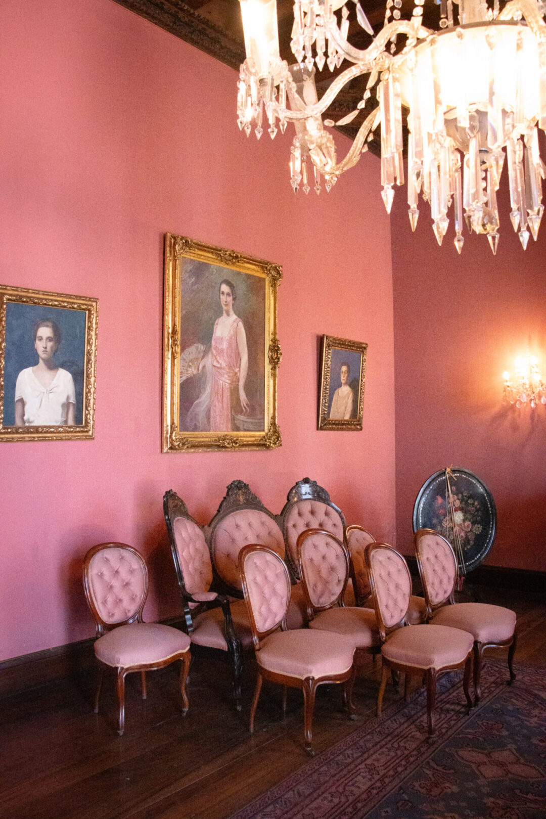 A pink dining room full of women's portraits and pink upholstered Victorian era chairs inside Casa de Larriva in Lima, Peru