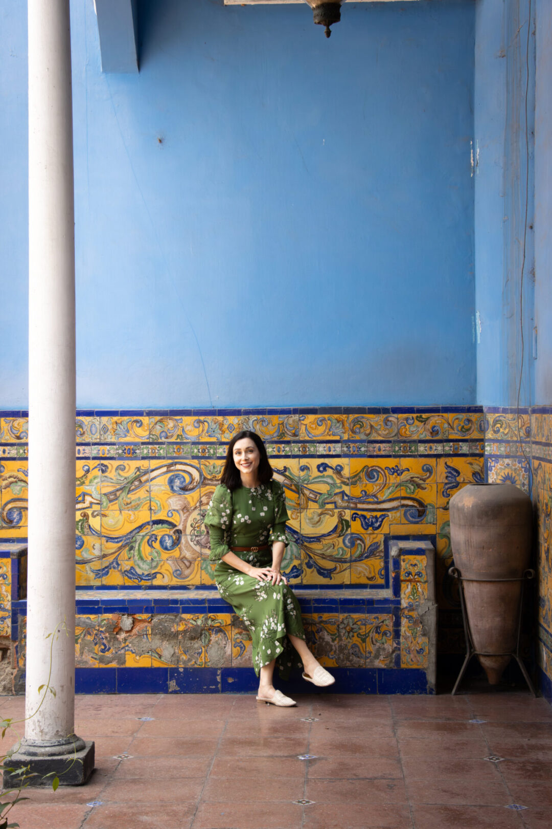 Travel Blogger Jordan Gassner smiling on a yellow tiled bench against a blue painted wall in the courtyard of Casa de Larriva in Lima, Peru