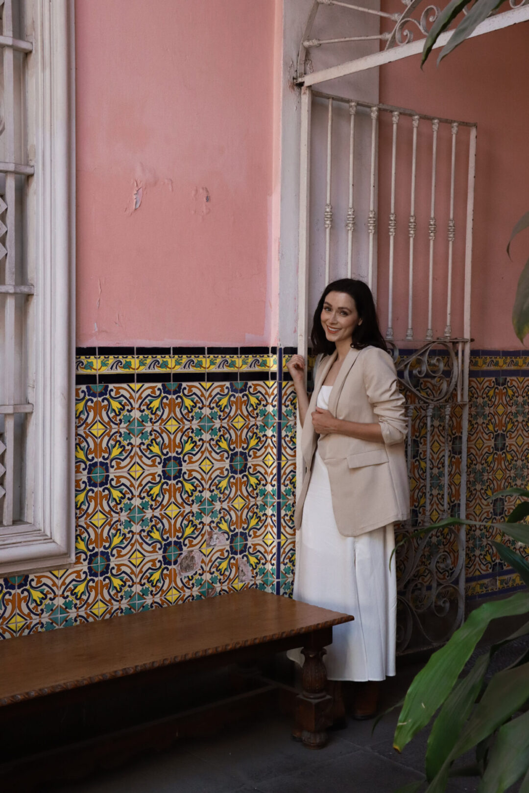 A woman smiling near a pink wall decorated with yellow, turquoise and blue tiles inside Casa de Osambela in Lima, Peru