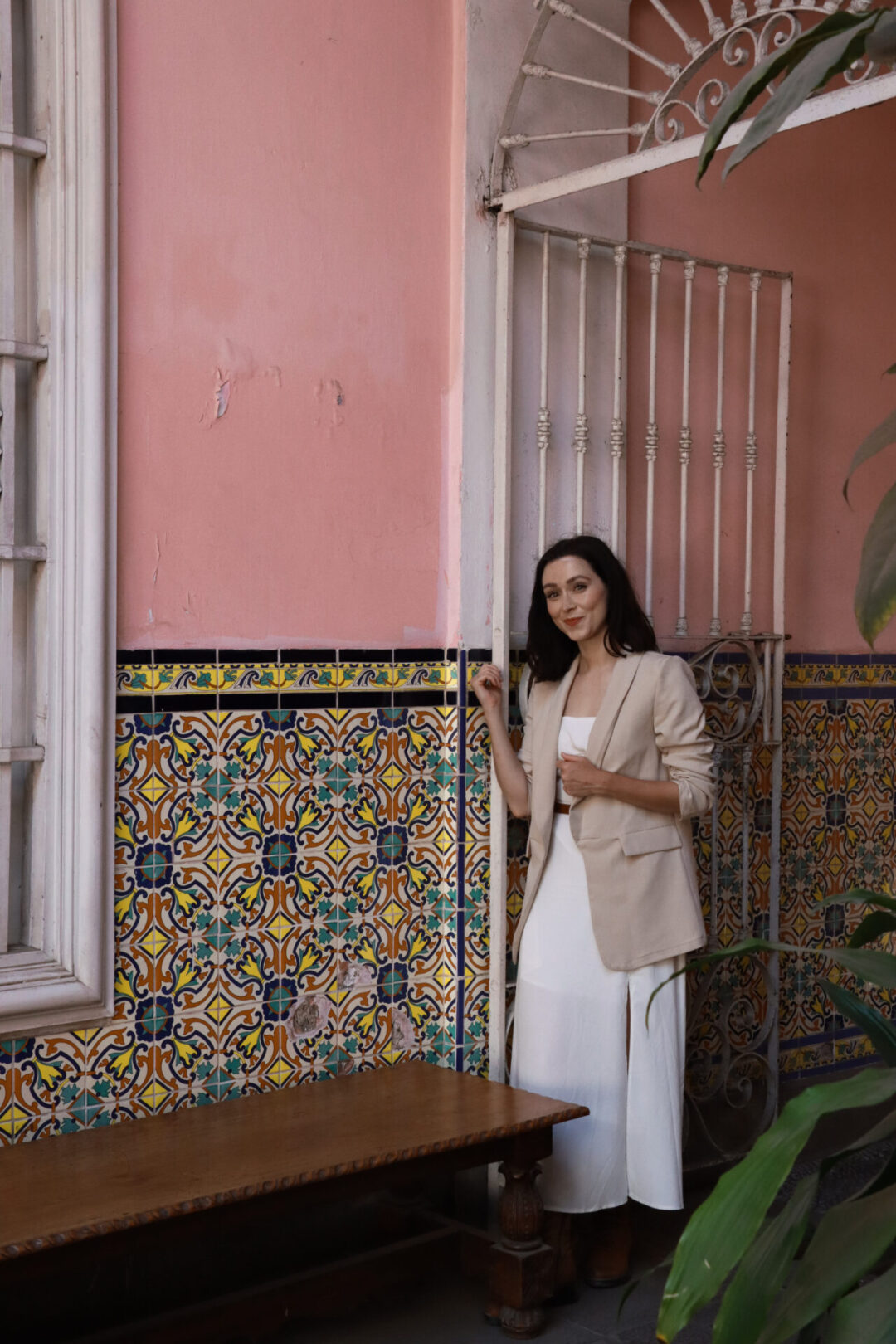 A woman standing near a pink wall decorated with yellow, turquoise and blue tiles inside Casa de Osambela in Lima, Peru