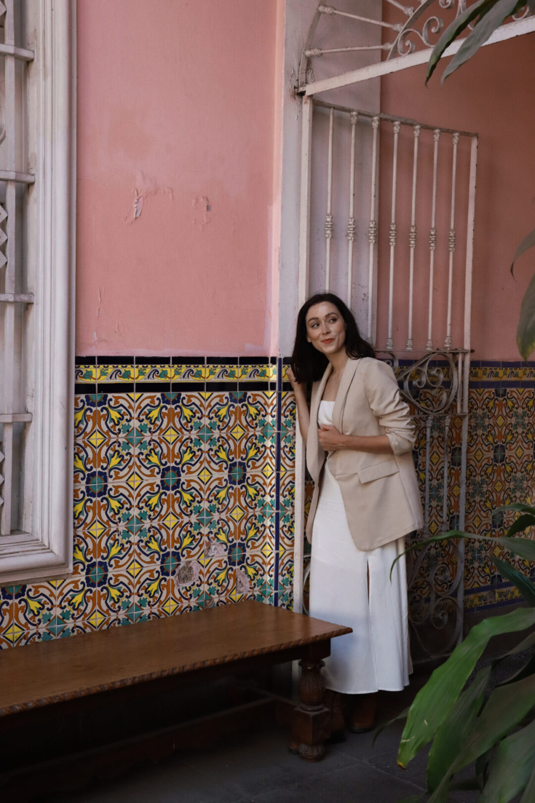 A woman looking over her shoulder near a pink wall decorated with yellow, turquoise and blue tiles inside Casa de Osambela in Lima, Peru