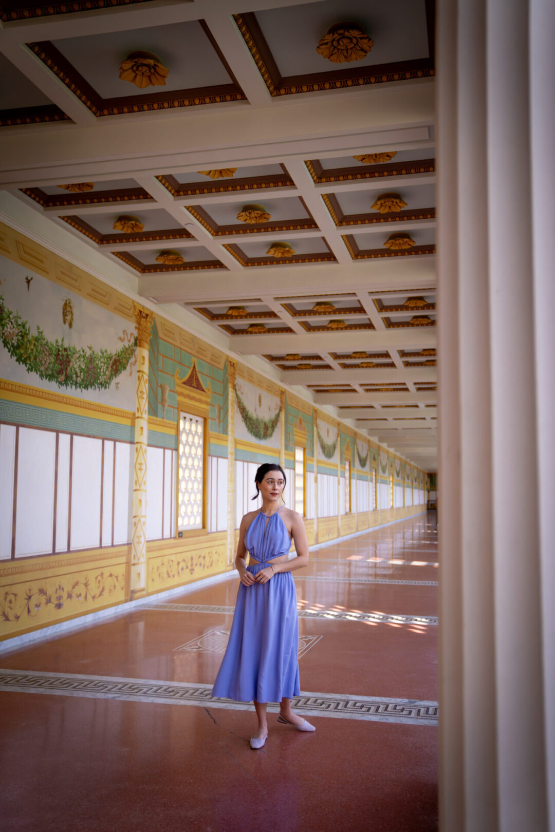 Travel Blogger Jordan Gassner wearing a purple dress under a colonnade in the garden of The Getty Villa in Los Angeles, California