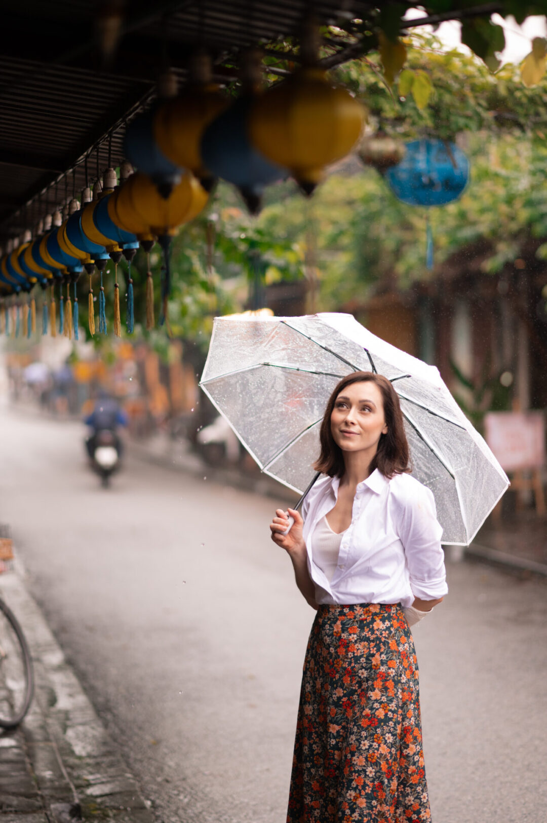 Travel Blogger Jordan Gassner looking up at some blue and yellow lanterns on a rainy day in Hoi An, Vietnam